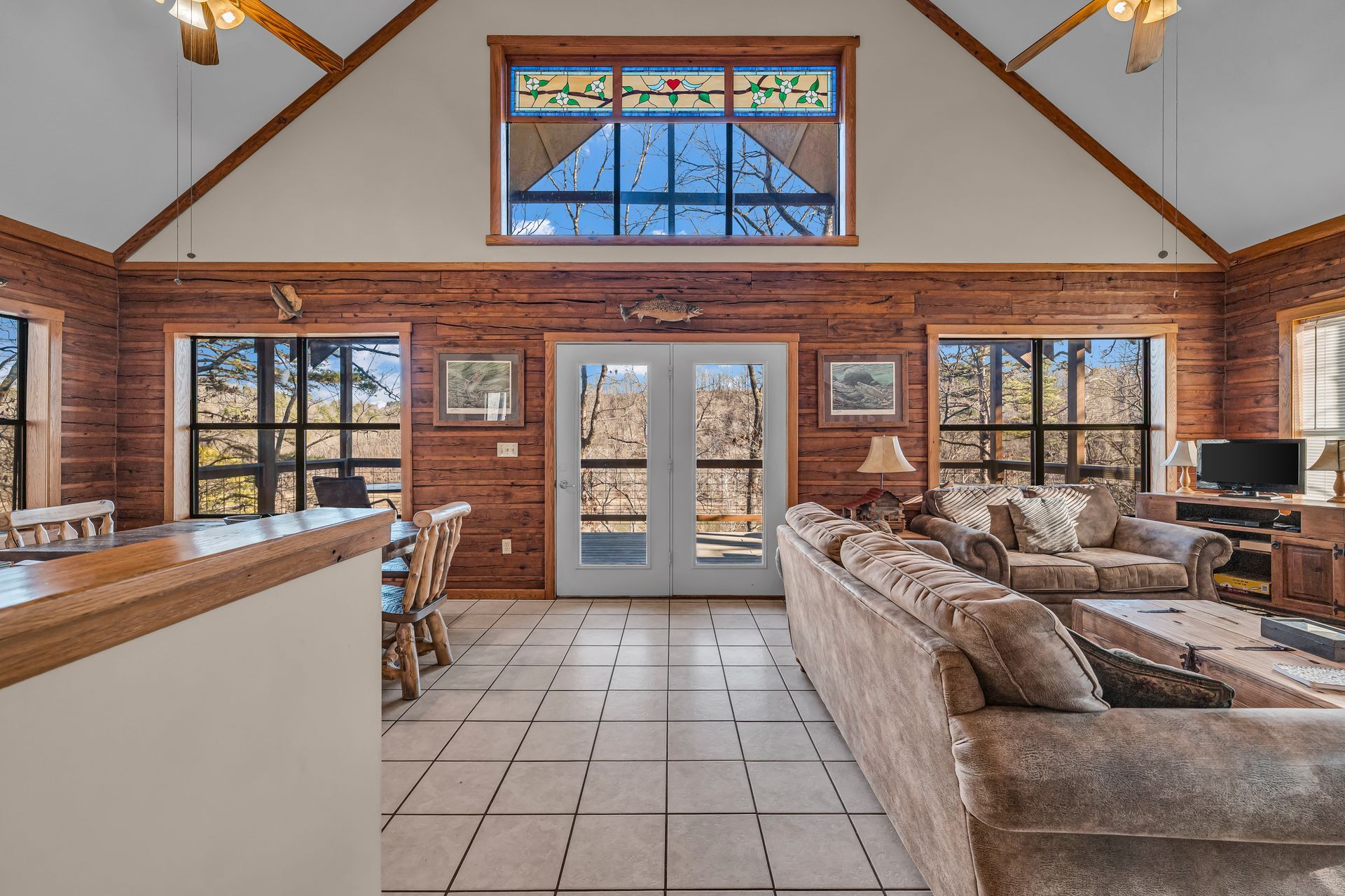 Spacious lodge lounge with stone fireplace, tan sofas, brick walls, and double glass doors under a vaulted ceiling