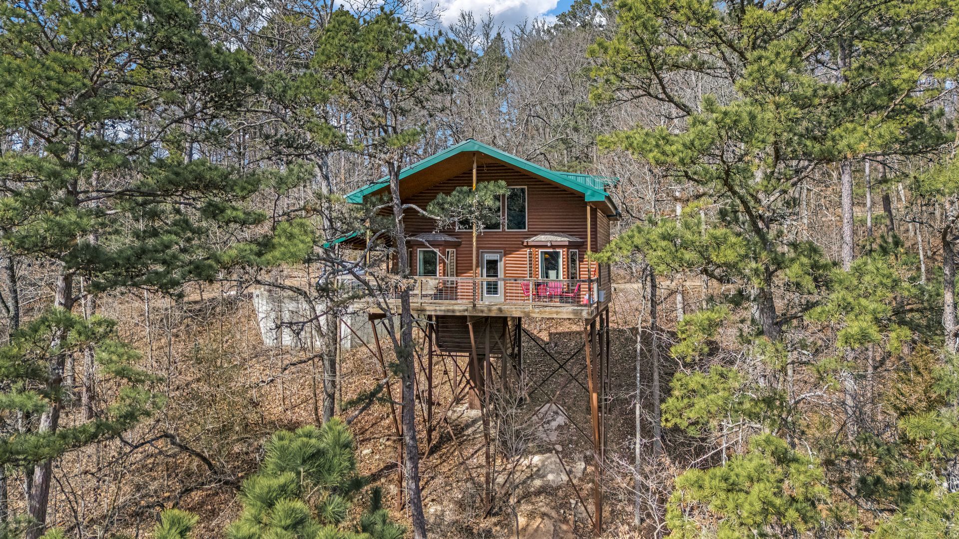 Small cabin with teal roof on a wooded hillside among leafless trees