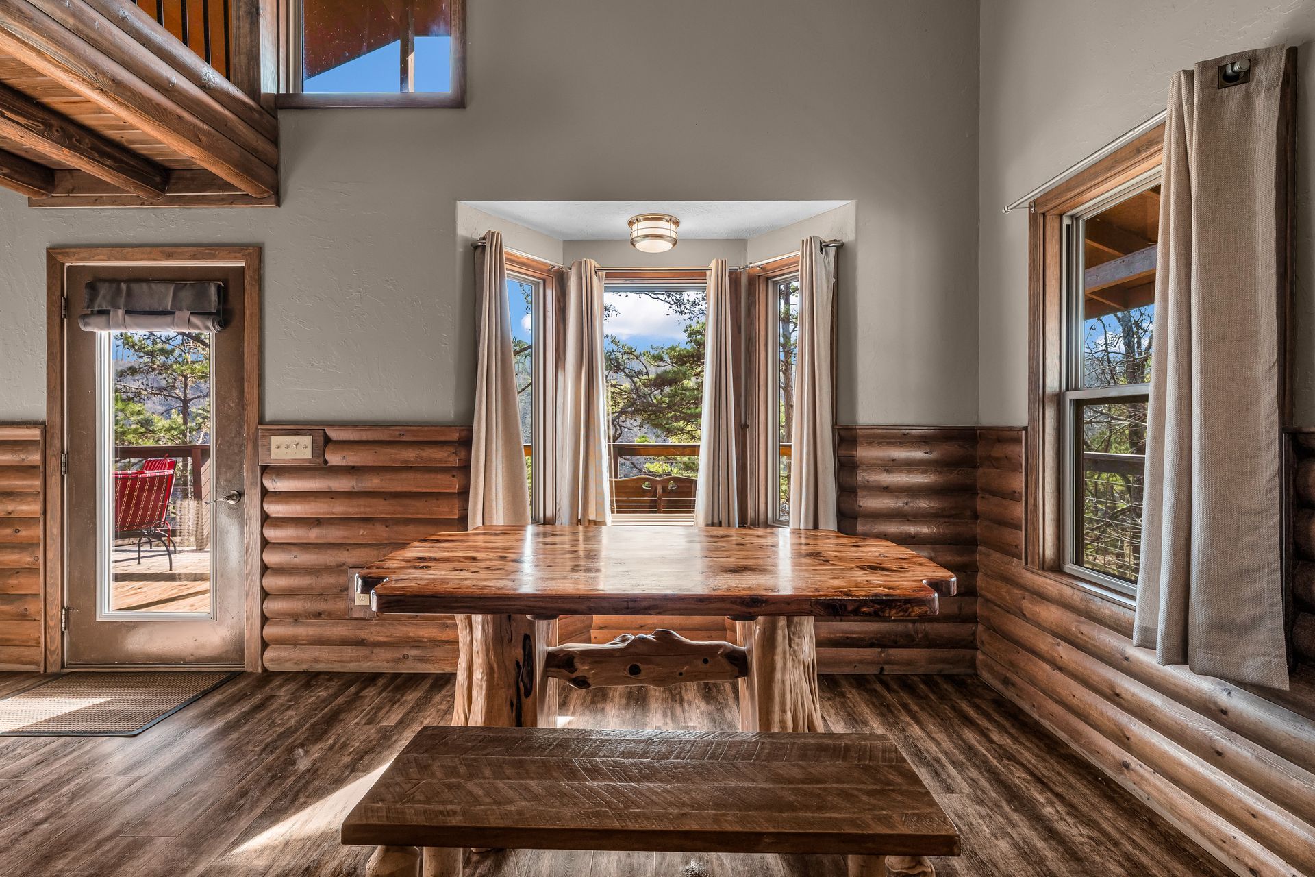 Rustic dining room with wooden table, benches, and open windows overlooking a scenic view