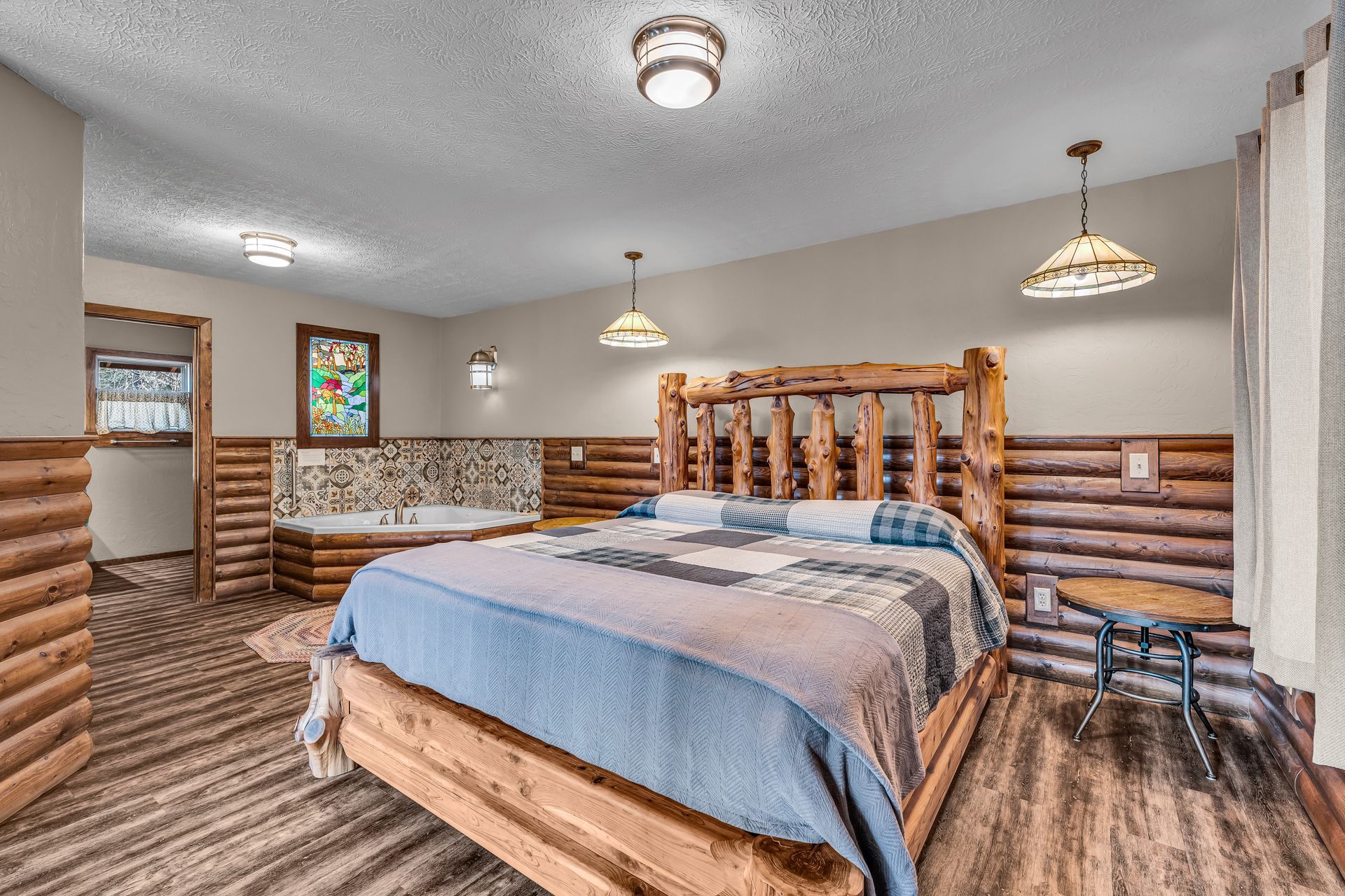 Rustic bedroom with log bed frame, blue bedding, wood-paneled walls, and ceiling lights