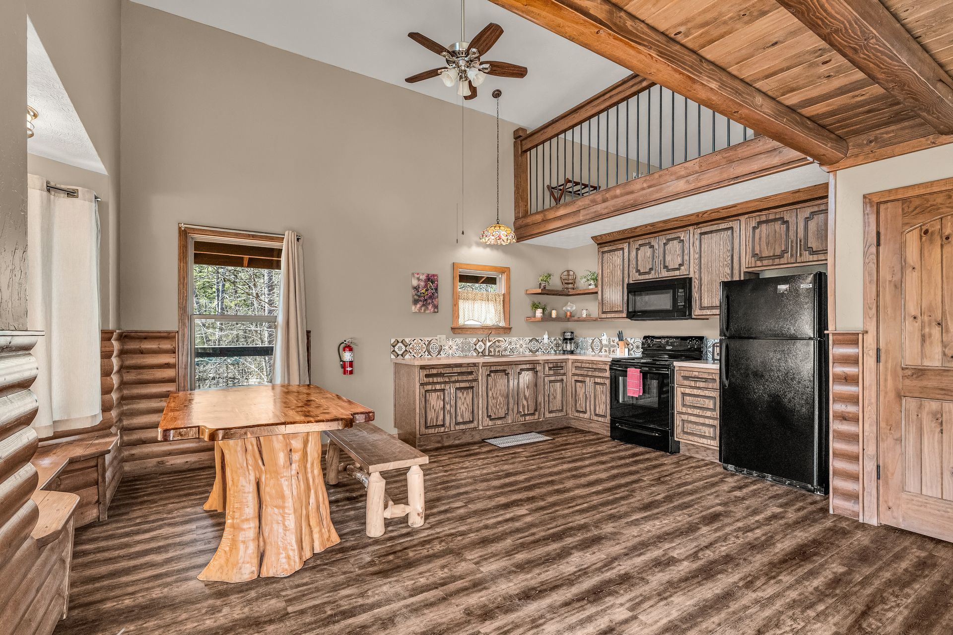 Rustic kitchen with wood beams, black appliances, staircase, and a small round table and stool.