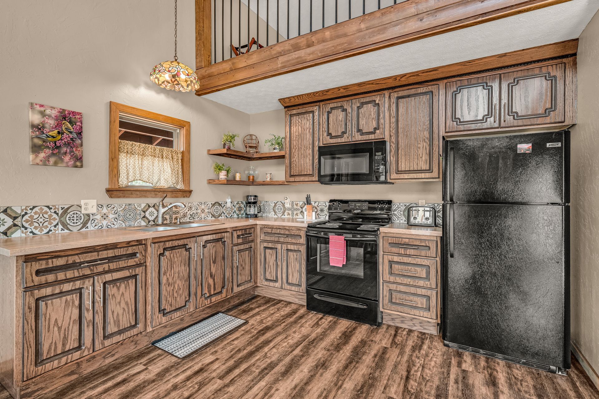 Modern kitchen with wood cabinets, black appliances, and a loft-style railing overhead.
