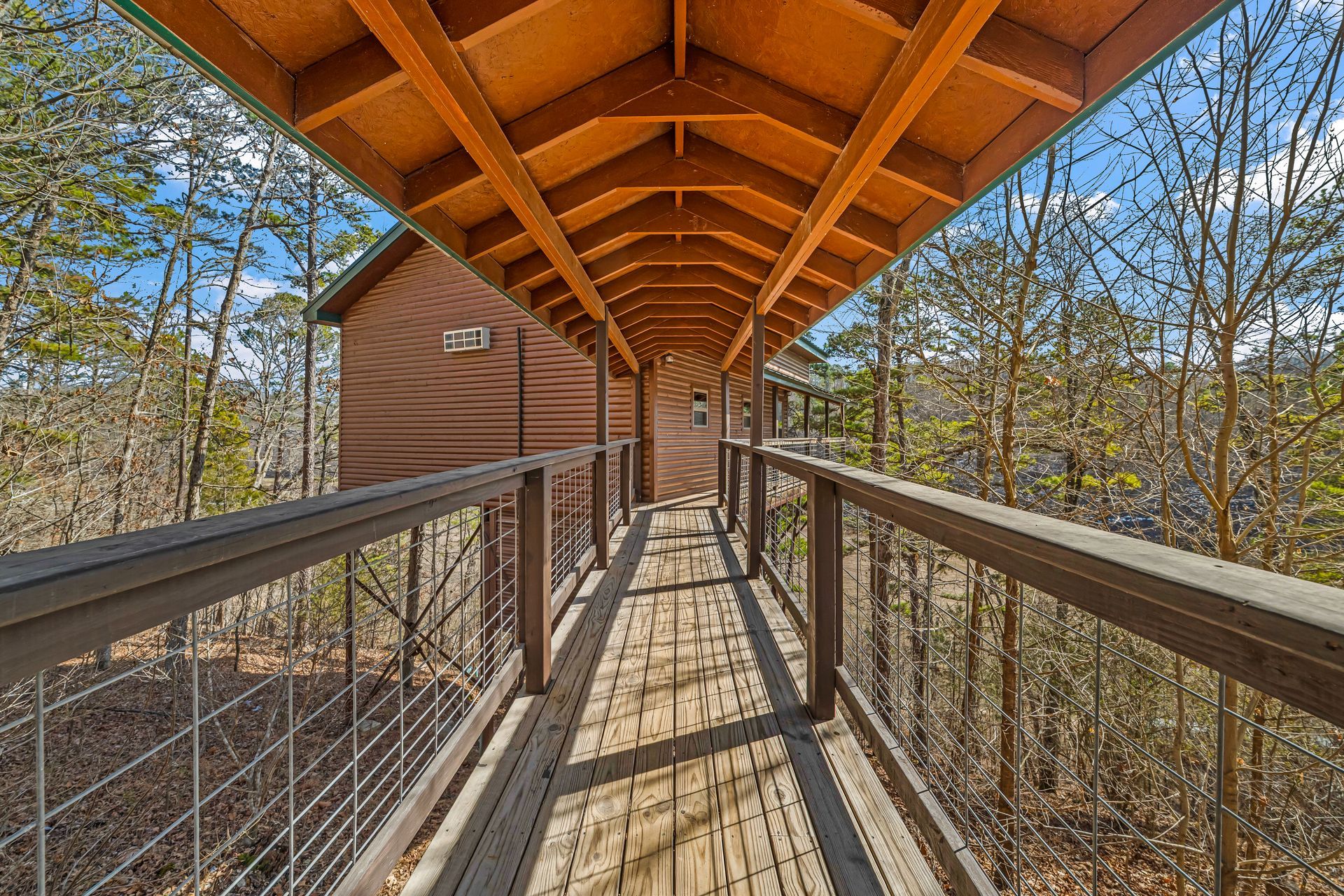 Covered wooden walkway with metal railings leading to a cabin in a wooded area