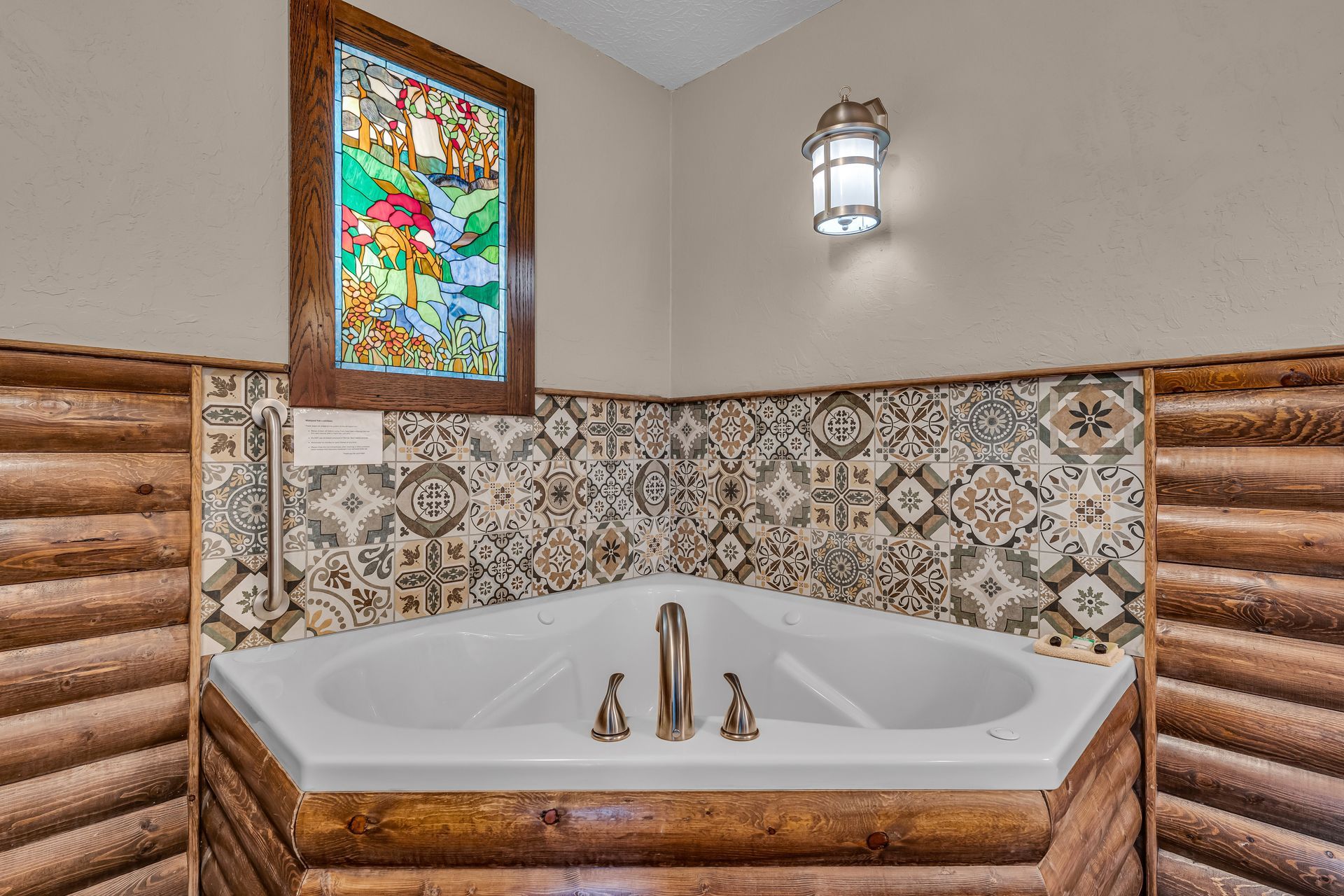 Corner soaking tub with bronze fixtures, ornate tile surround, wood paneling, and a stained-glass window
