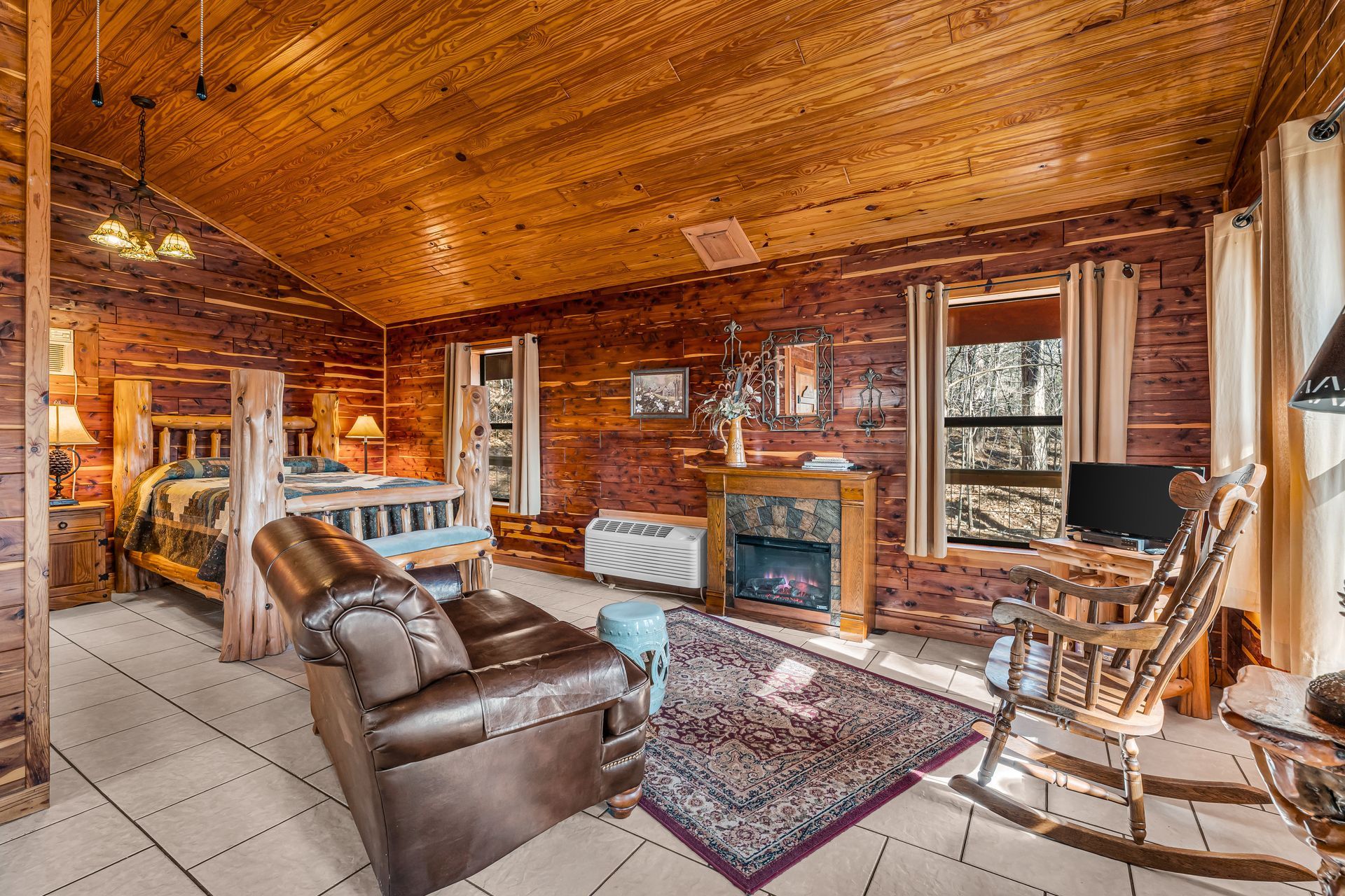 Cozy rustic living room with wood-paneled walls, tiled floor, leather sofa, fireplace, and rocking chairs