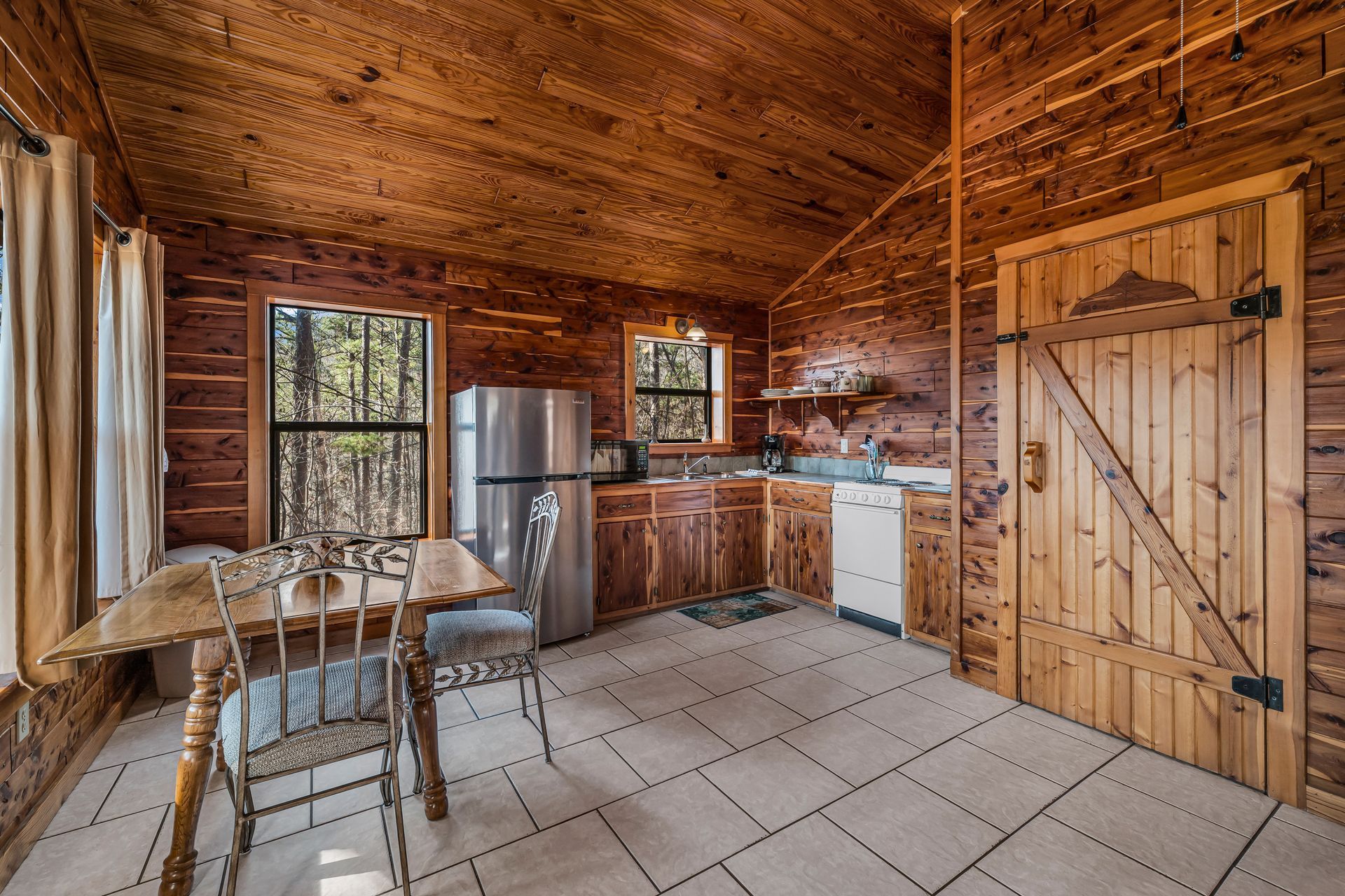 Rustic wooden kitchen with tiled floor, table, chairs, cabinets, sink, and refrigerator