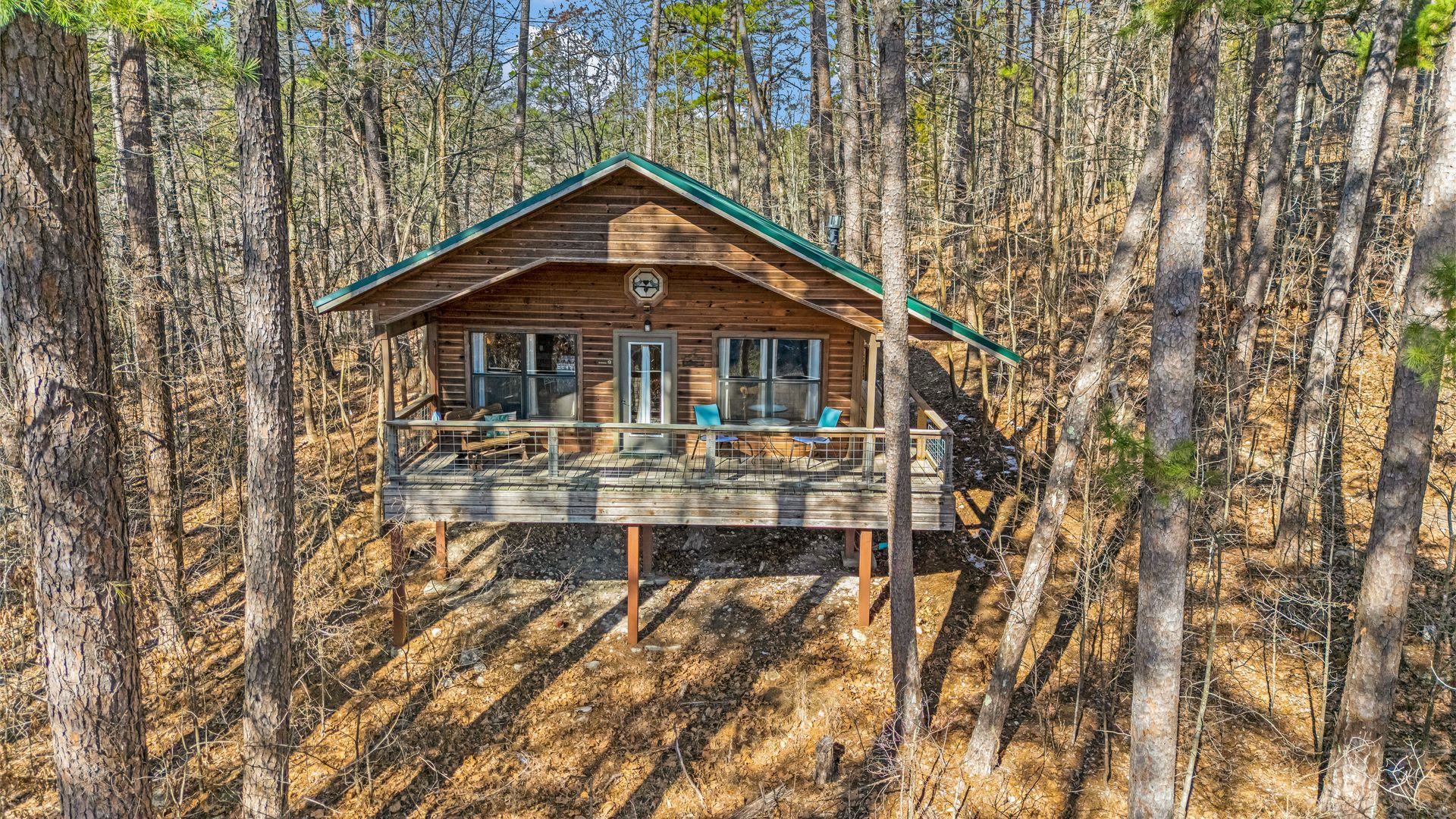 Wooden cabin with a wraparound deck nestled among leafless trees in a forest