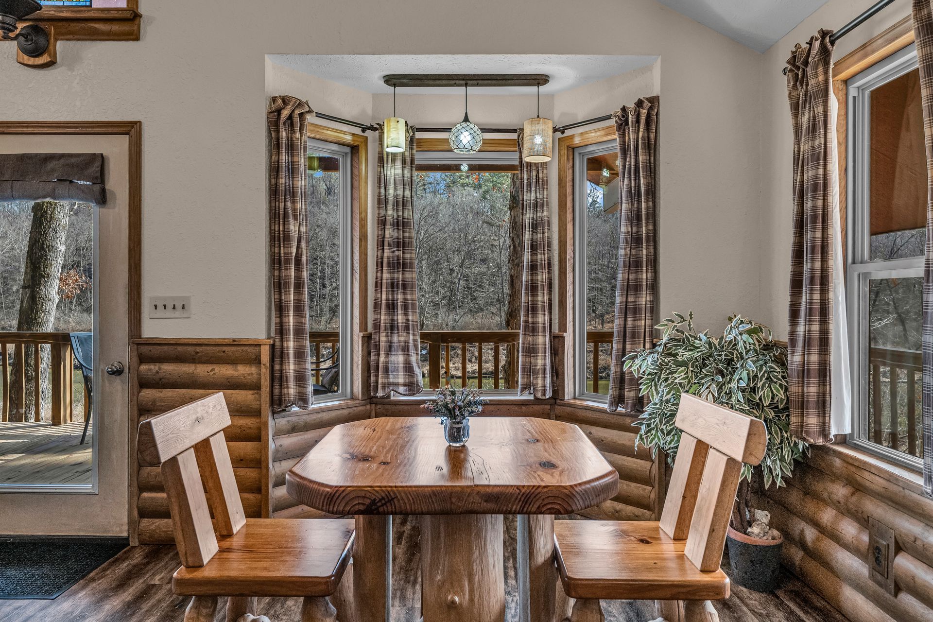 Wood-paneled dining nook with a wooden table, benches, and large windows looking out onto trees.