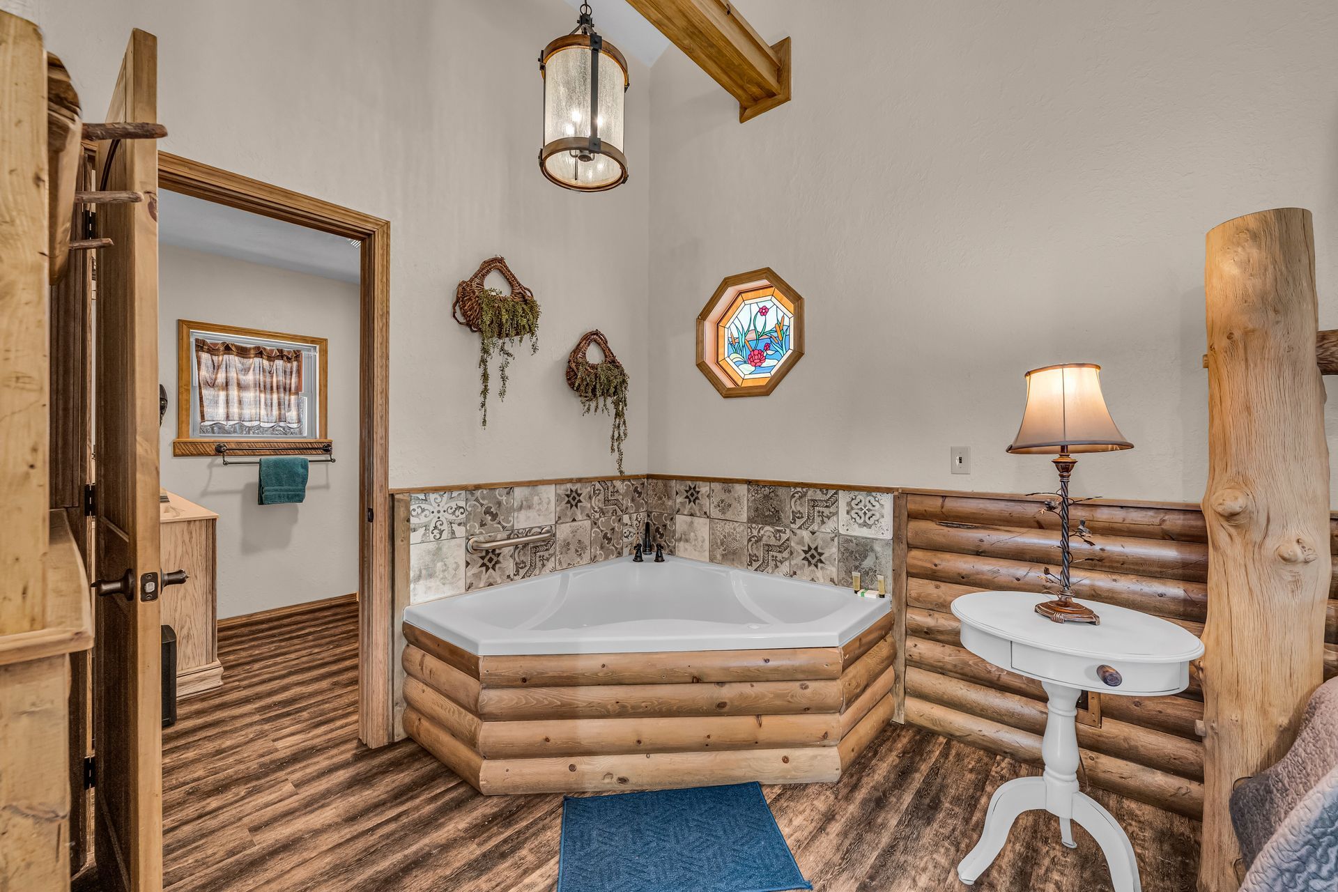 Rustic bathroom with octagonal tub, log walls, patterned tile, and a small side table lamp