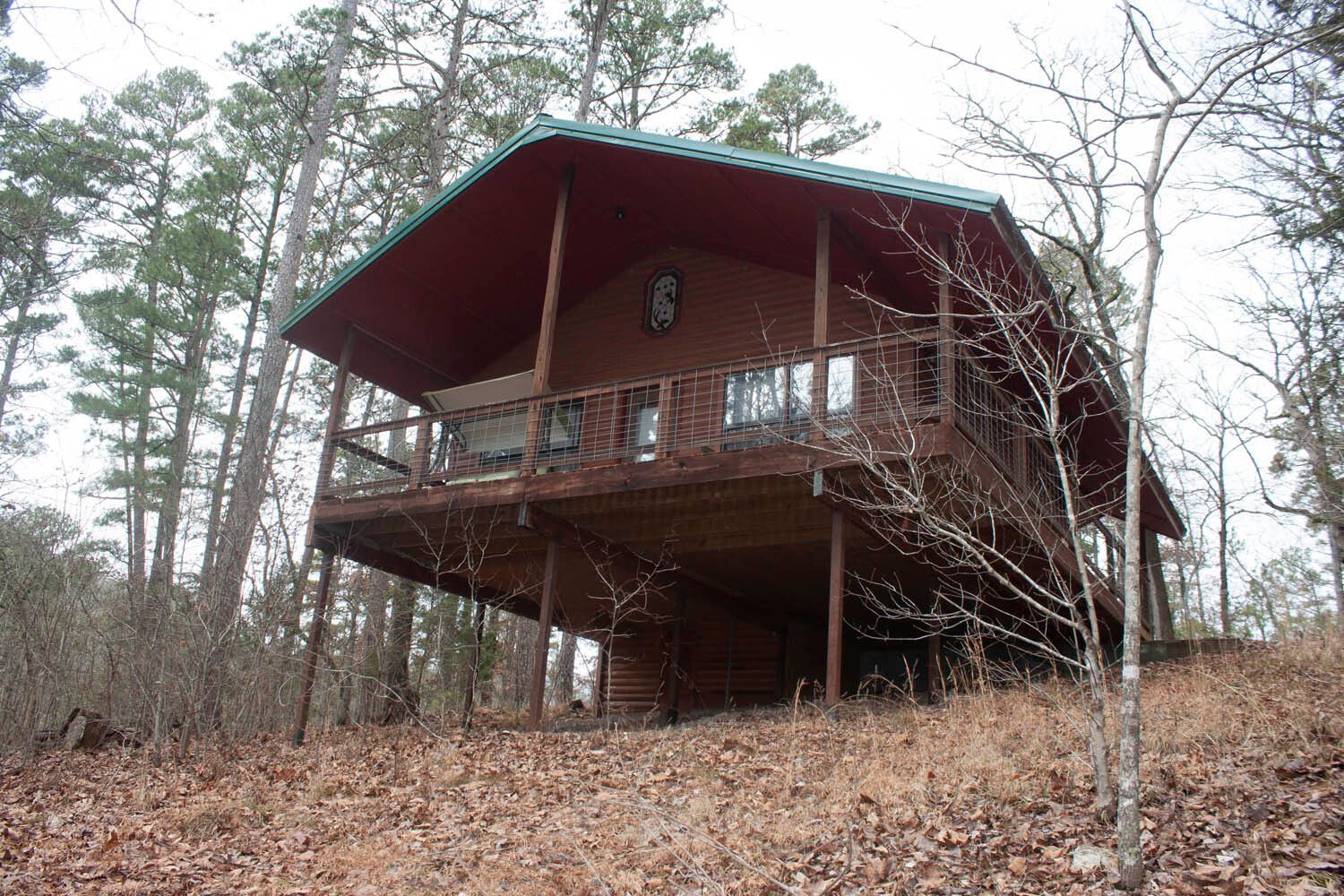Wooded hillside cabin with a red roof and elevated wooden deck among bare trees