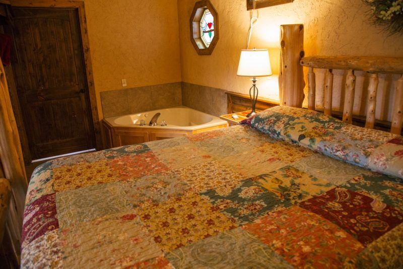 Cozy bedroom with patchwork quilt, wooden bed, lamp, and a corner bathtub by the wall