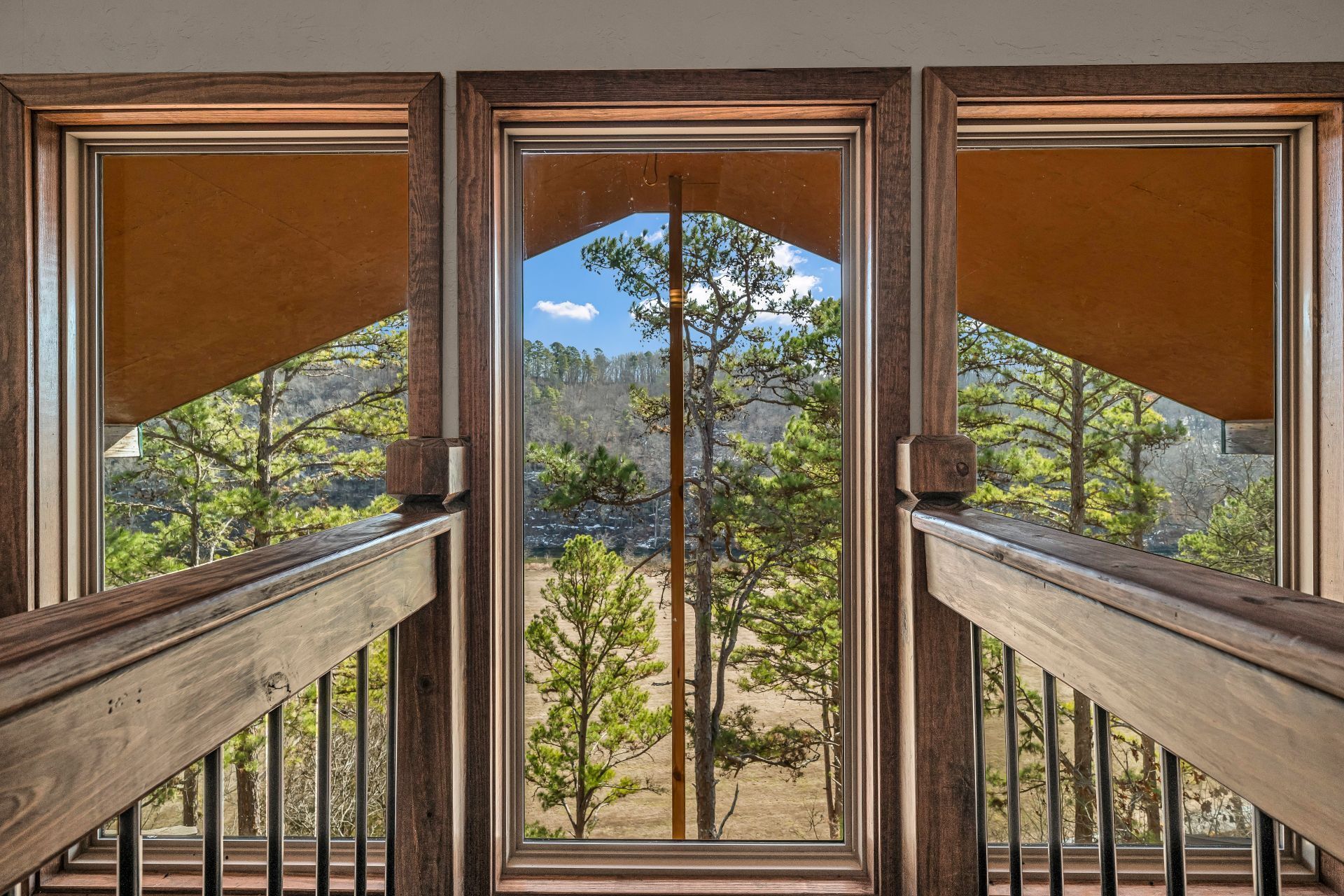 Wooden balcony framing a glass door view of pine trees and mountains under a clear sky