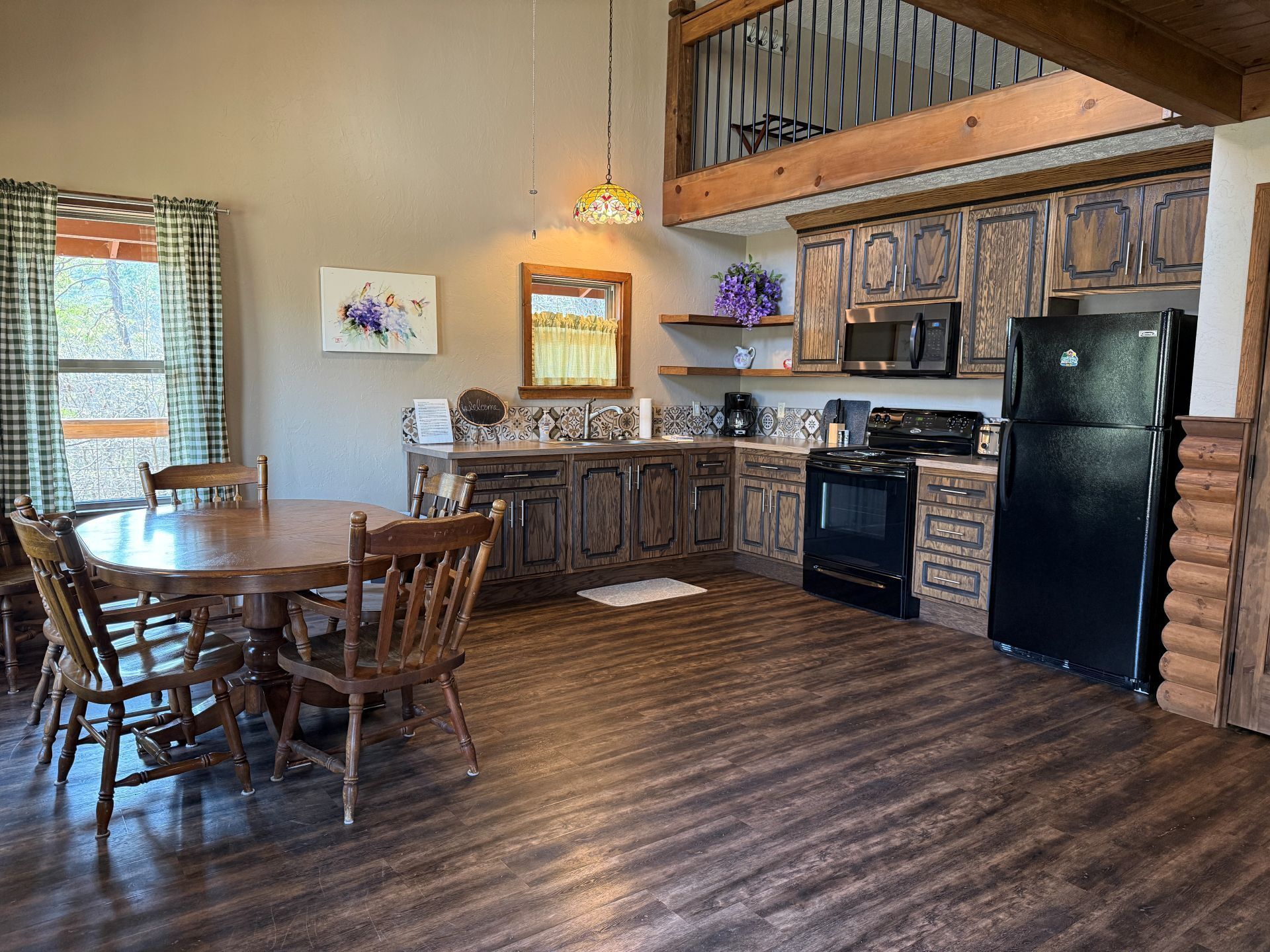 Rustic kitchen with wood cabinets, black appliances, dining table, and staircase loft.