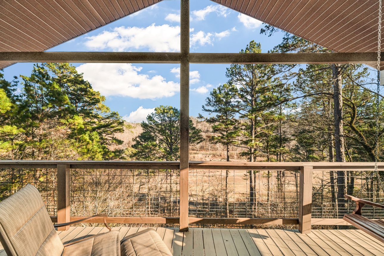 Wooden deck with lounge chair and railing overlooking trees under a slatted pergola roof