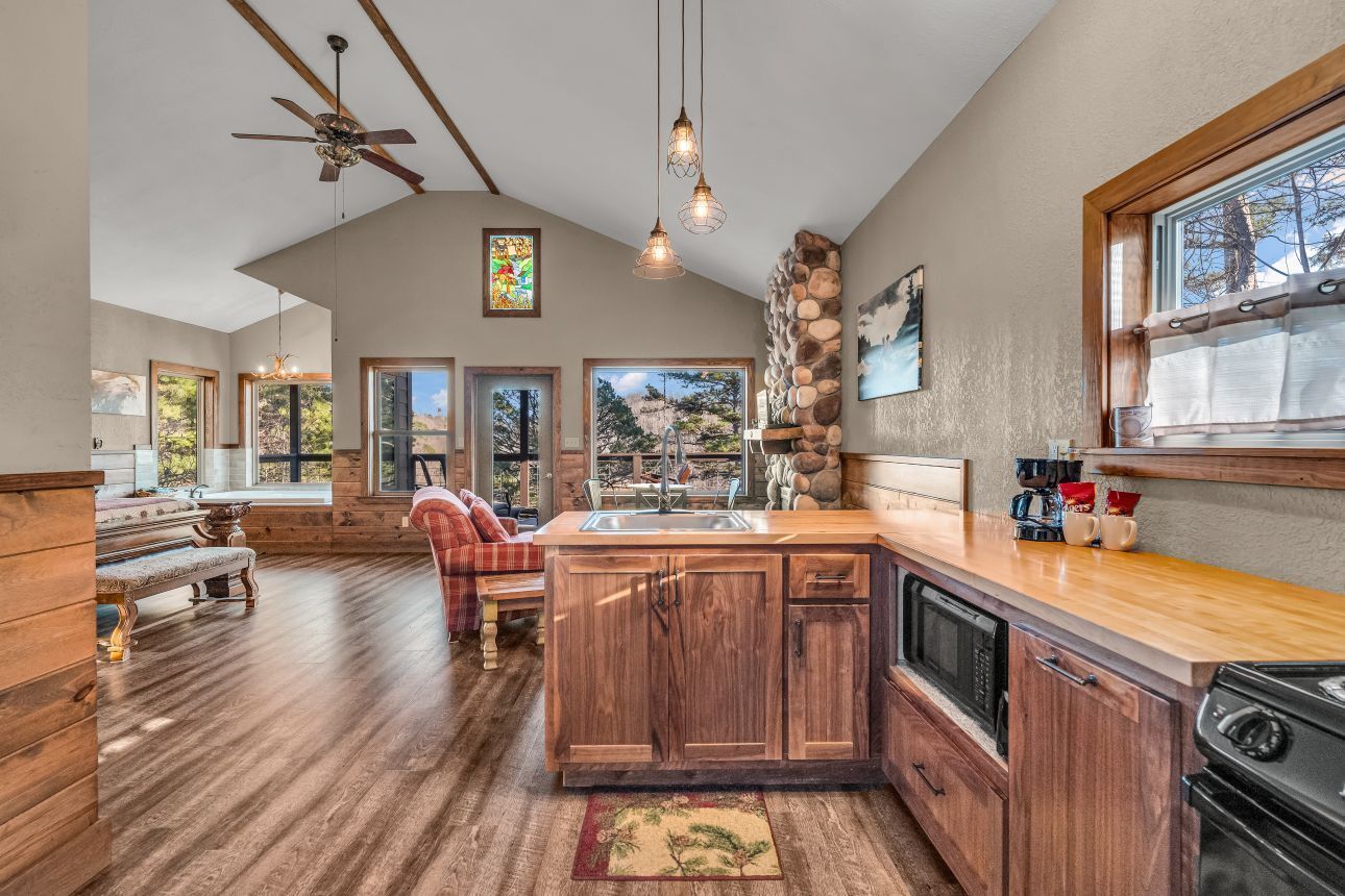 Bright open kitchen with wood floors, rustic cabinets, island, pendant lights, and large windows overlooking trees