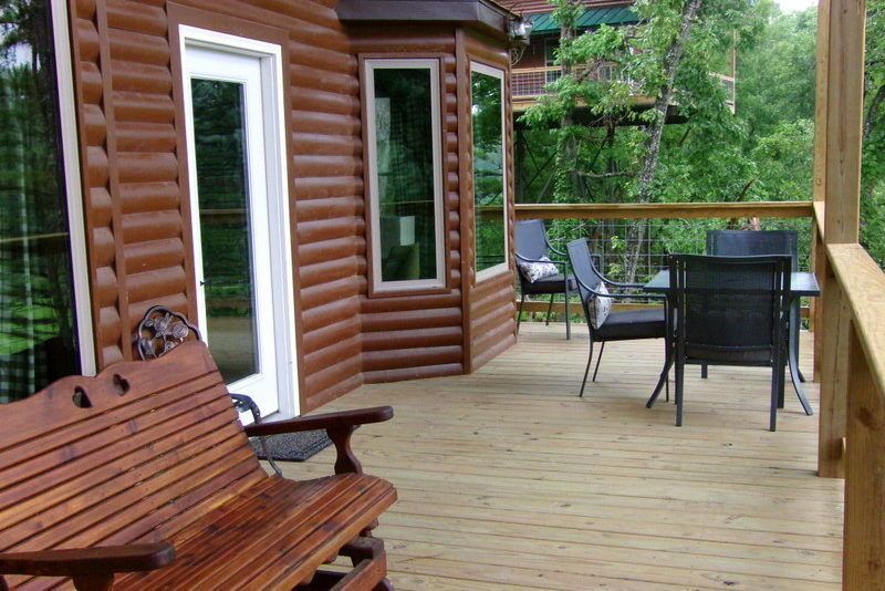 Wooden cabin deck with bench, patio table, chairs, and forest view