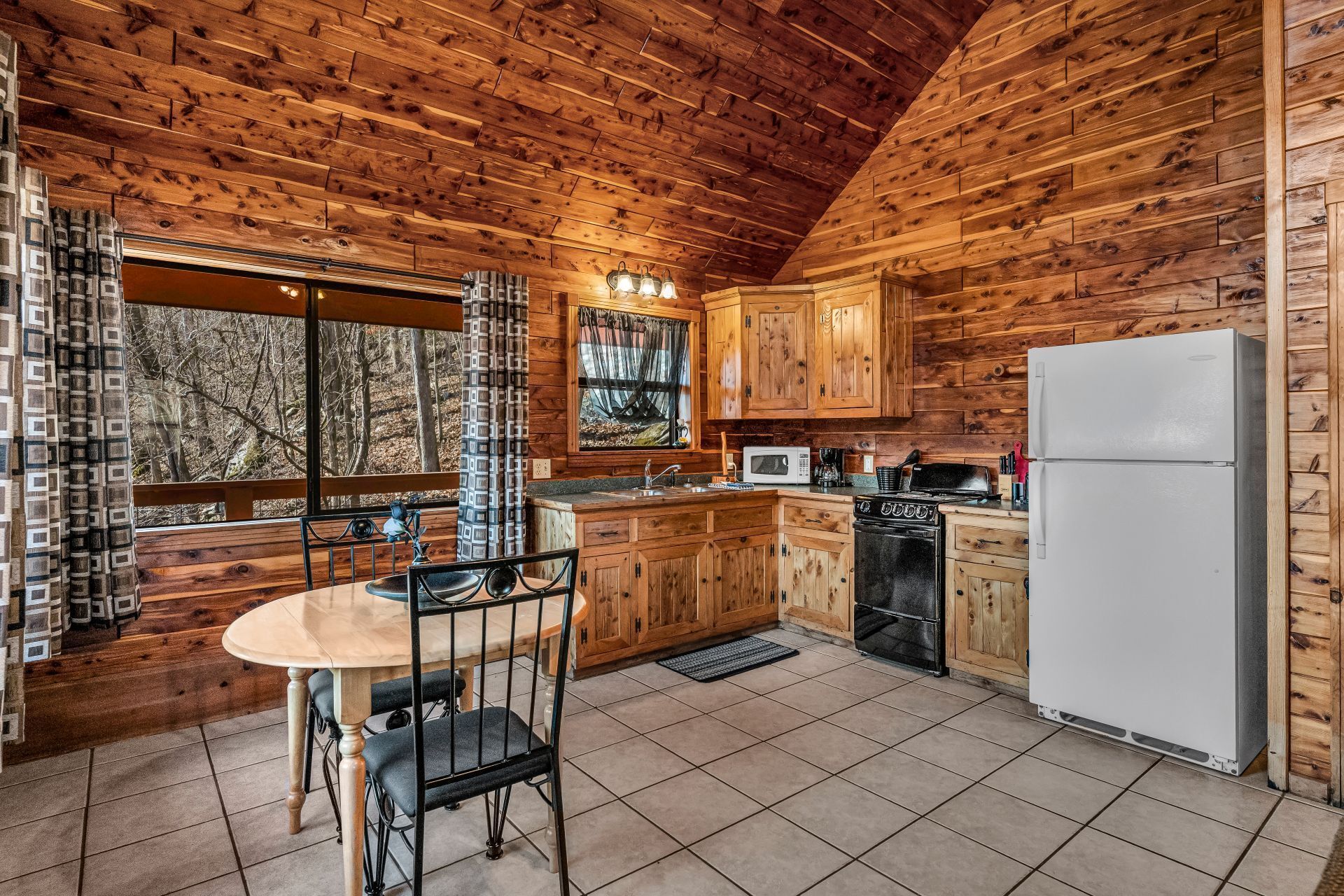 Cozy wood-paneled kitchen with tiled floor, round table, stove, cabinets, and white refrigerator