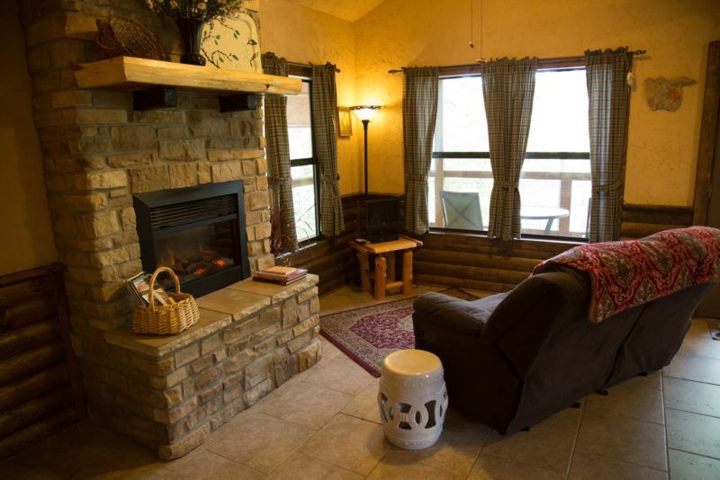 Cozy living room with stone fireplace, leather sofa, lamp, and large windows with curtains