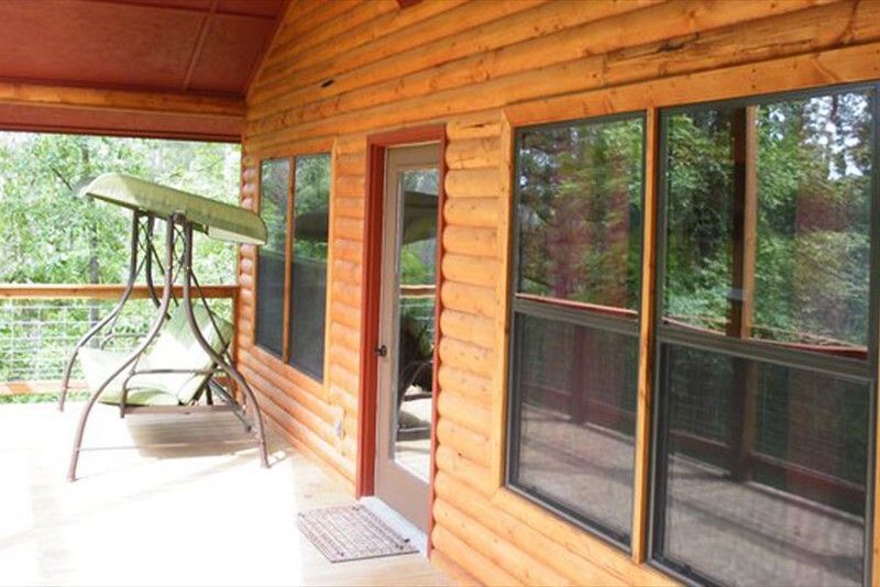 Covered wooden porch with windows and a hanging swing bench overlooking trees