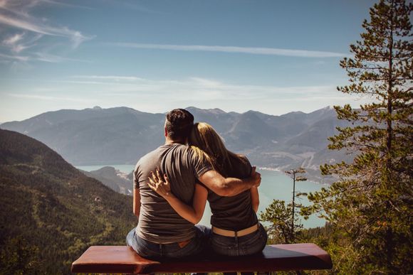 Couple sitting on a bench overlooking a lake and mountains at sunset