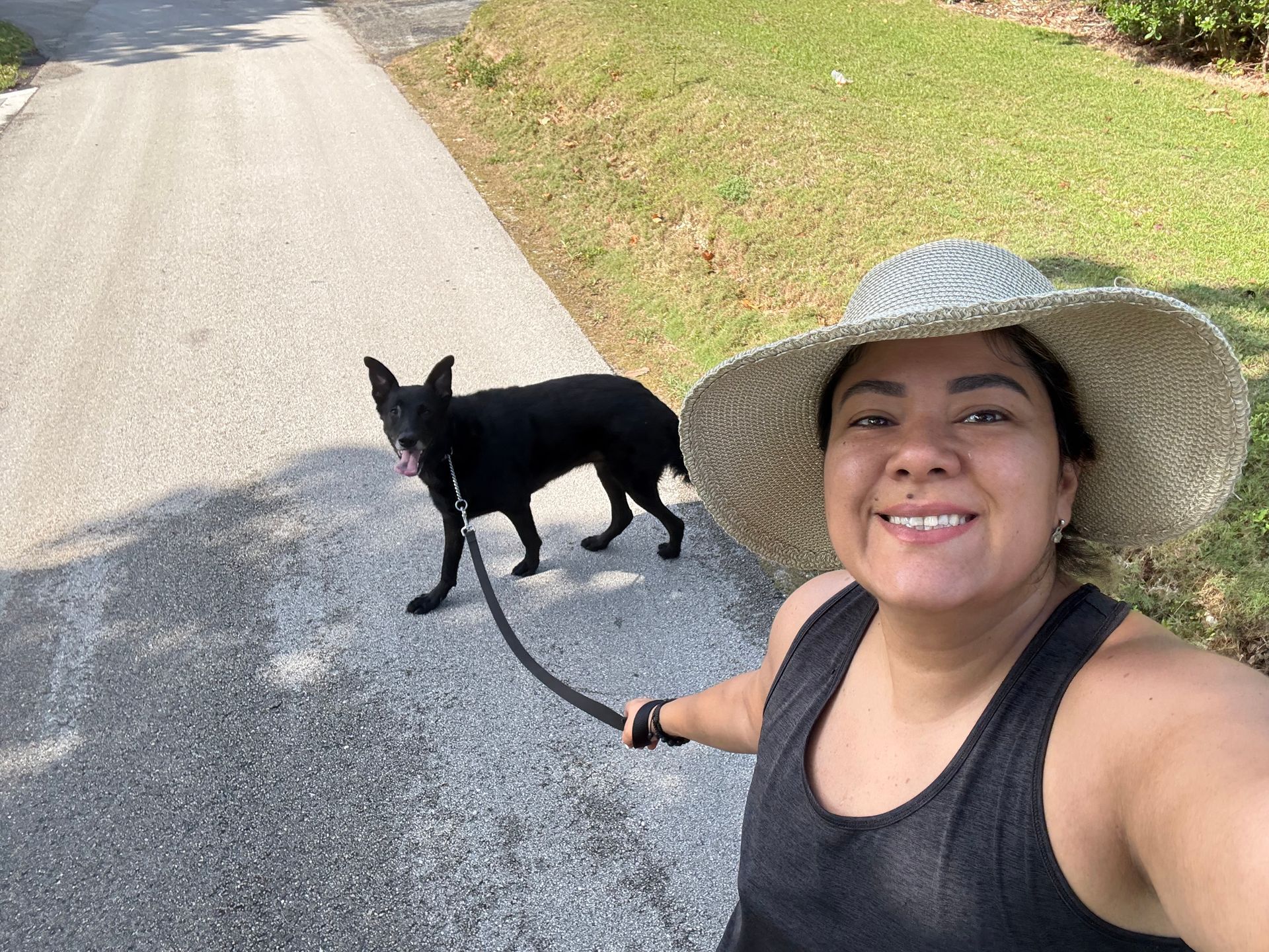 A woman wearing a hat is walking a black dog on a leash