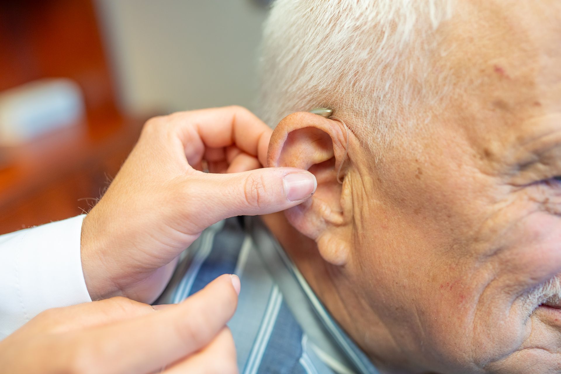 A person's ear being fitted with a hearing aid by a hand.
