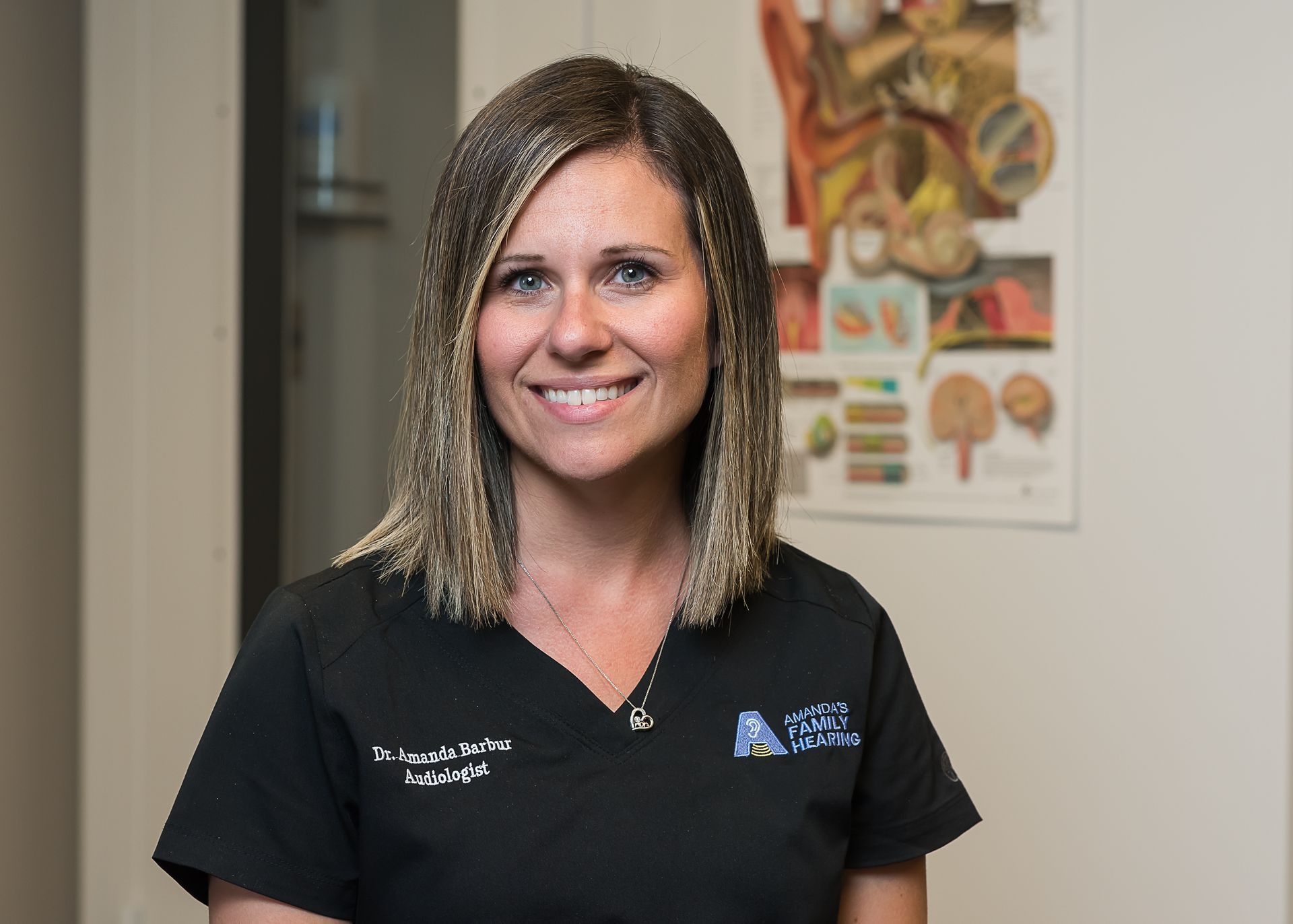 Woman in black scrubs smiles at camera, medical office setting.