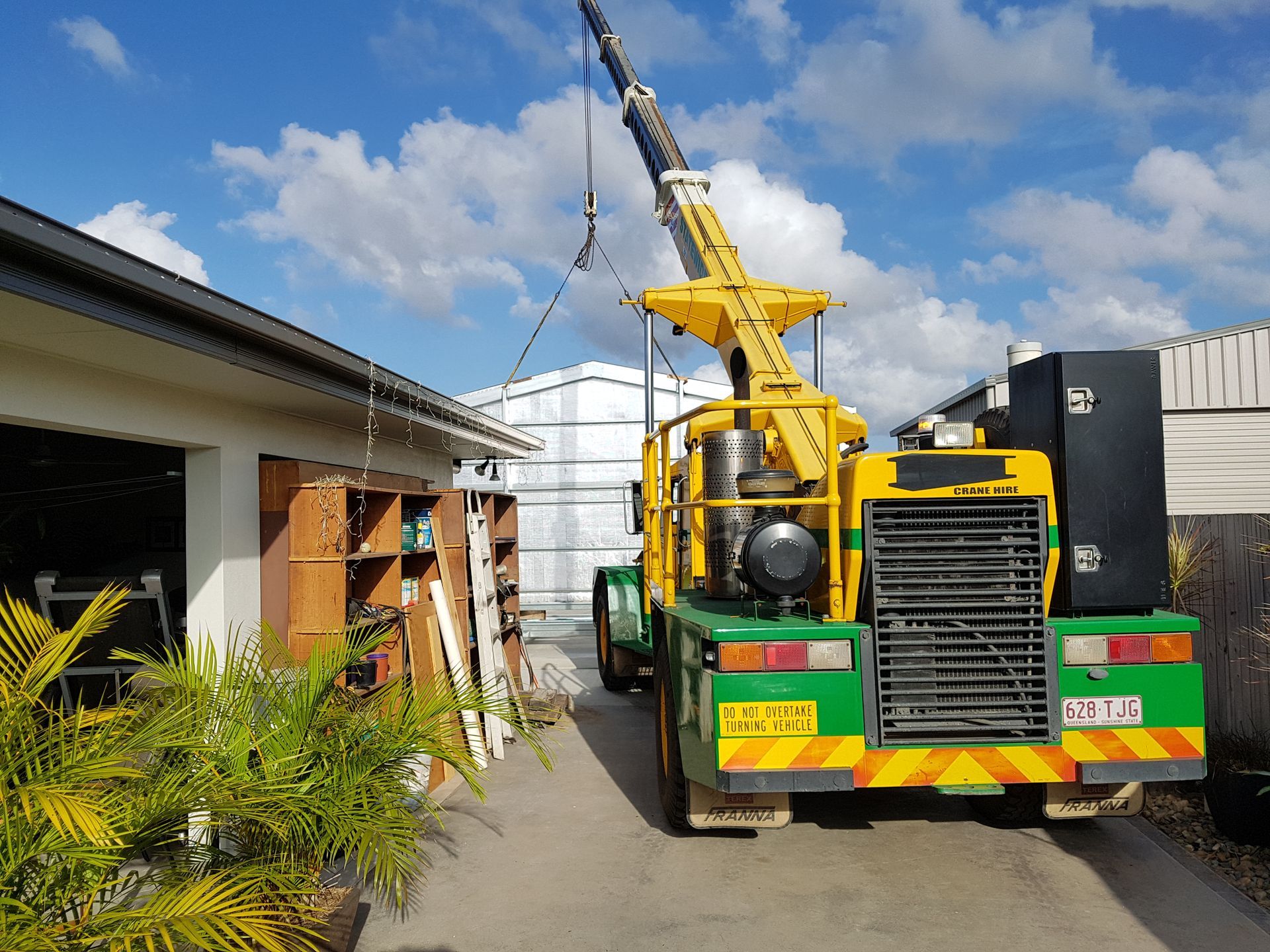Yellow crane lifting a load near a building, sunny day — Statewide Lift & Shift Pty Ltd In Paget, QLD
