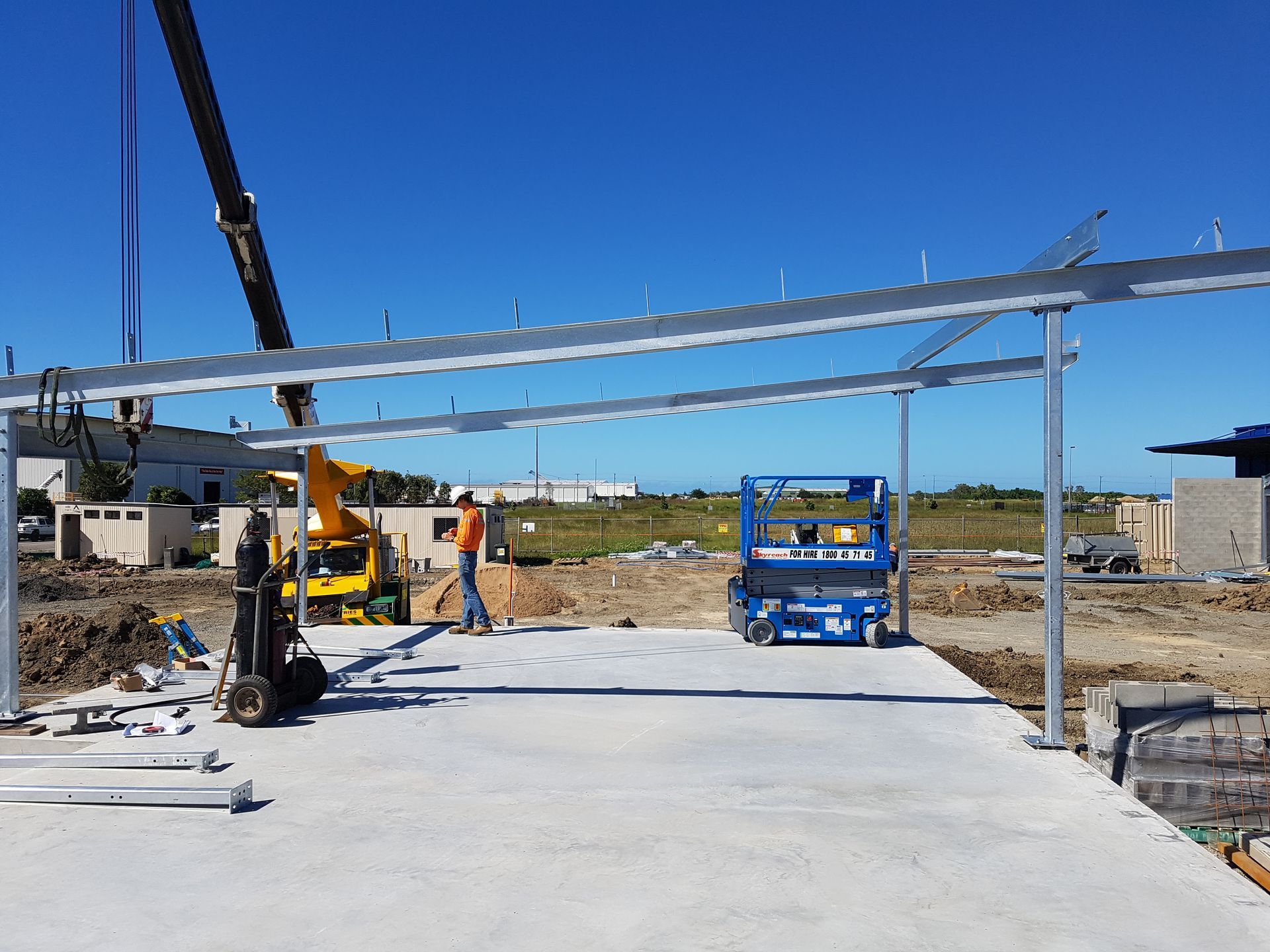 Construction site: metal frame being erected over a concrete slab. A worker stands nearby— Statewide Lift & Shift Pty Ltd In Paget, QLD