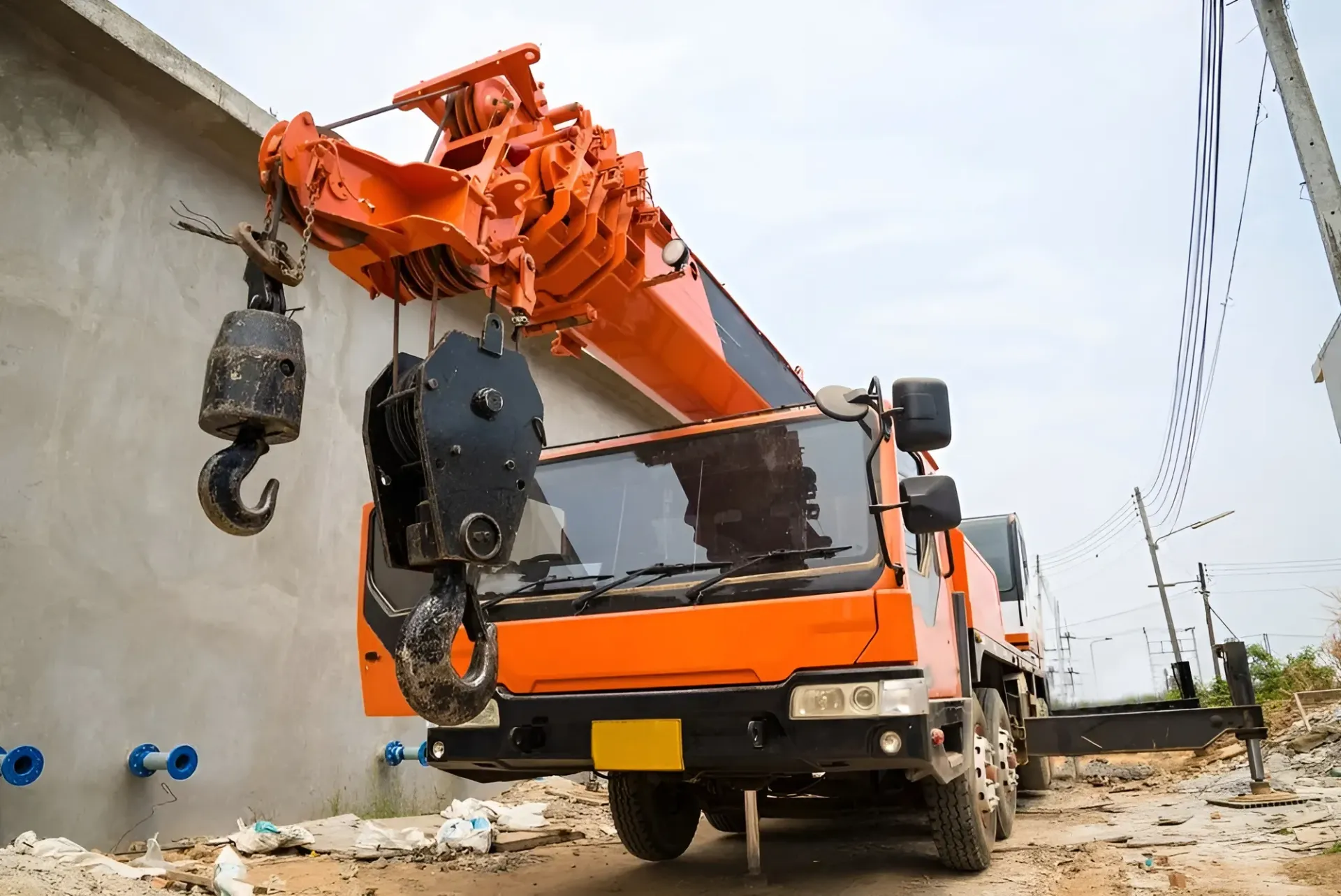 Orange crane truck lifting near a gray wall with blue pipes — Statewide Lift & Shift Pty Ltd In Sarina, QLD