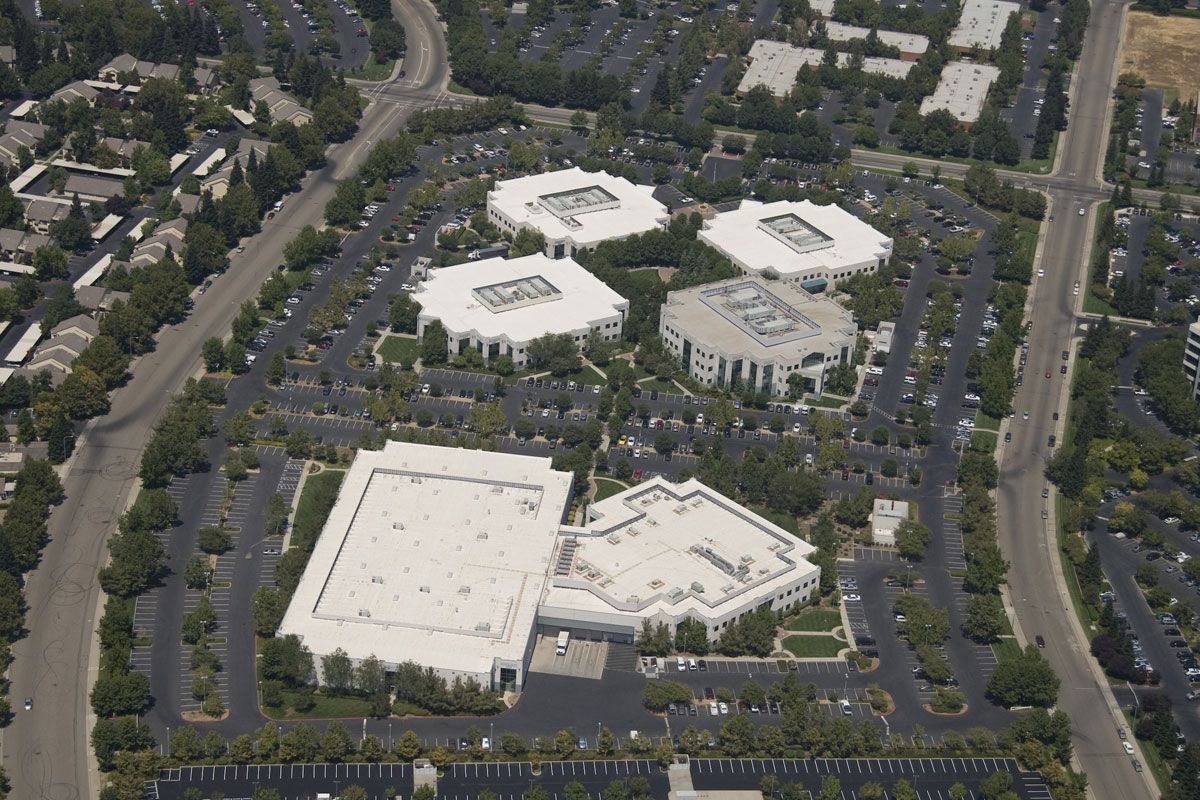 An aerial view of a corporate office complex with several white buildings surrounded by parking lots and trees.