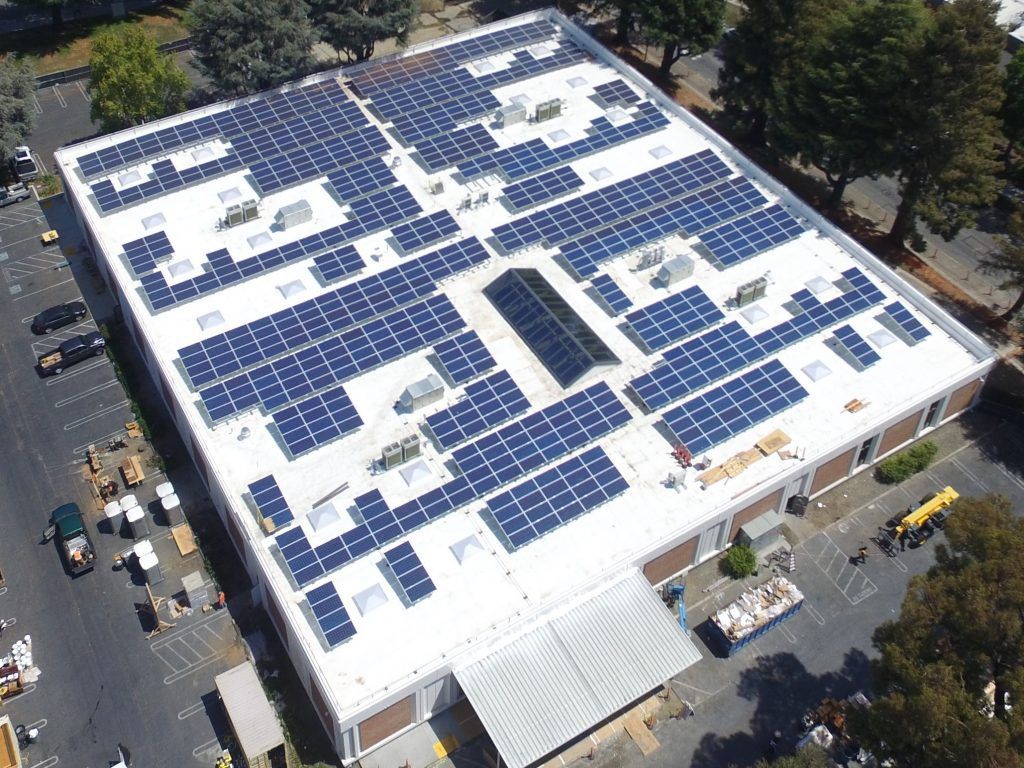 An aerial view of a large flat commercial building roof covered with extensive solar panel arrays.