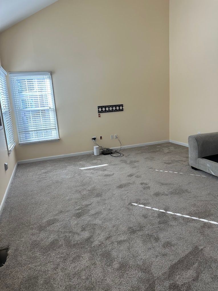 An empty room with beige walls, high ceilings, gray carpet, a window with blinds, and media wall connections.