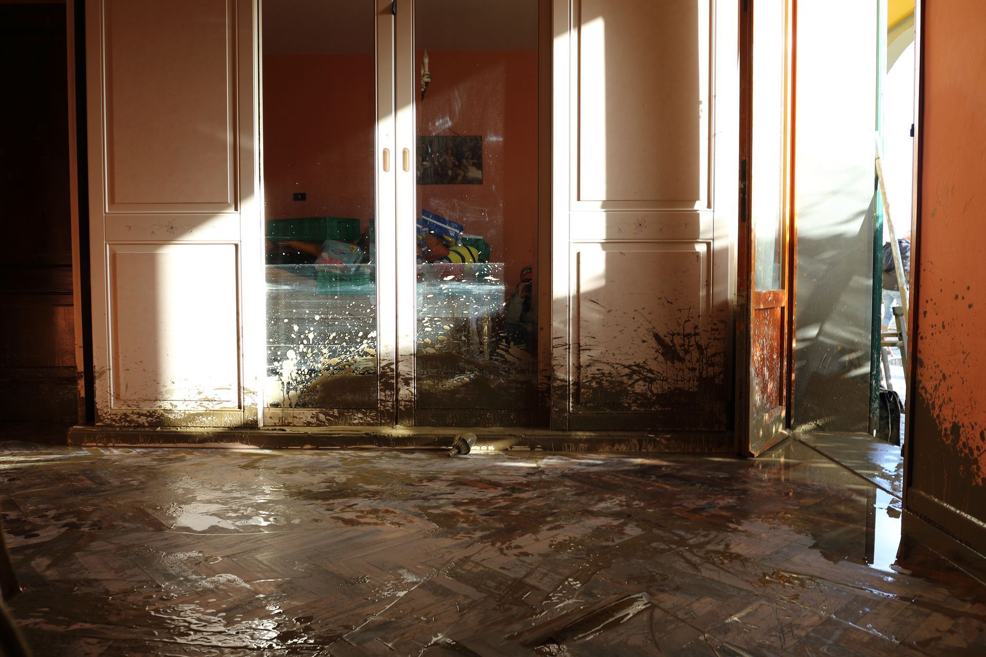 A room interior covered in dark mud and water after a flood, showing mud-splattered walls and a debris-strewn floor.