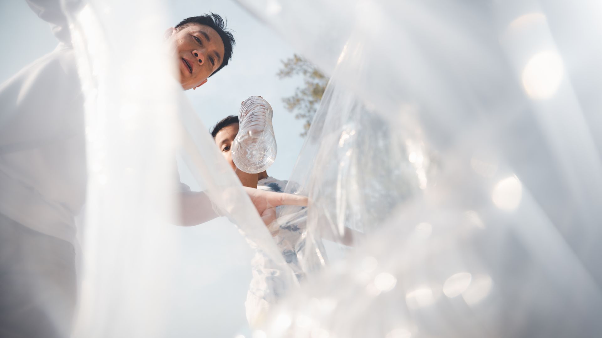 Two people in light clothing seen from a low angle through flowing, translucent white fabric.