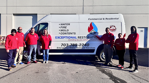 Eight people in red shirts stand in a line in front of a white restoration service van in a parking lot.