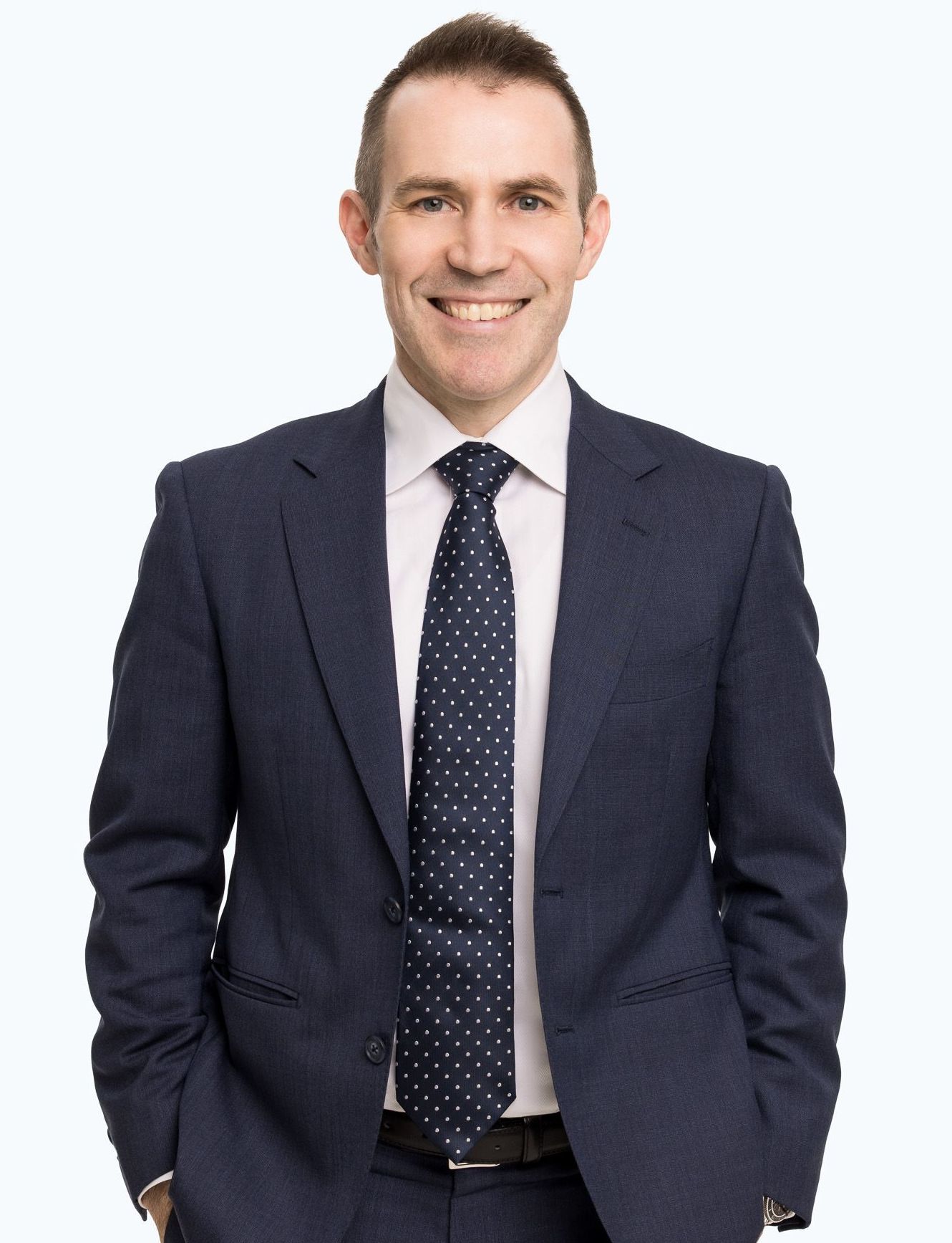 A man in a suit and tie is smiling with his hands in his pockets.