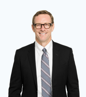 A man in a suit and tie is smiling with his hands in his pockets.
