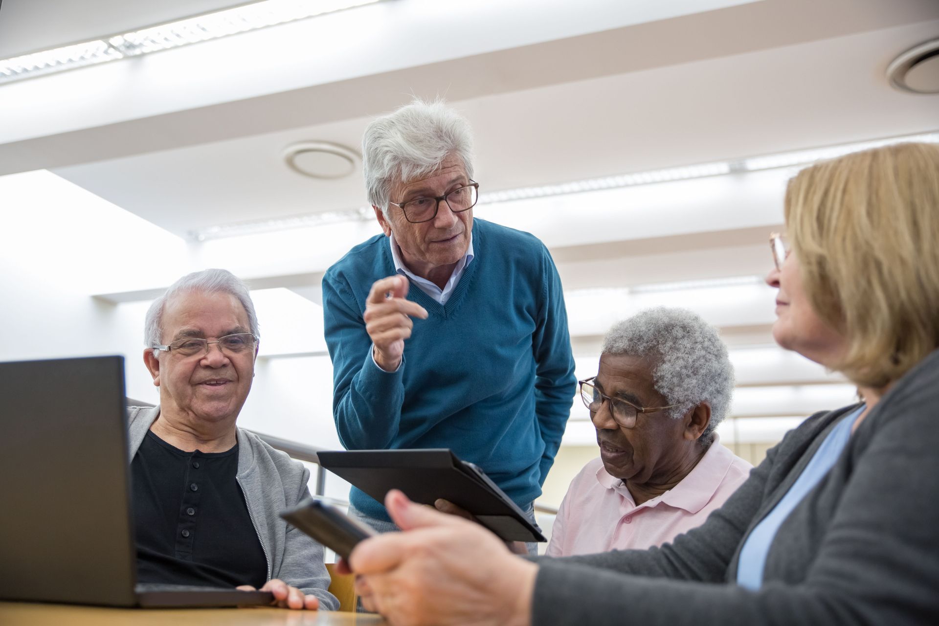 Small group in discussion, one person standing and pointing at a tablet in a bright meeting room.