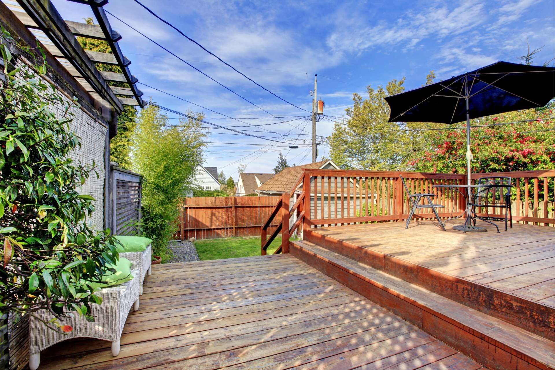 Wooden deck with outdoor furniture, umbrella, and a view of a yard with a wooden fence.