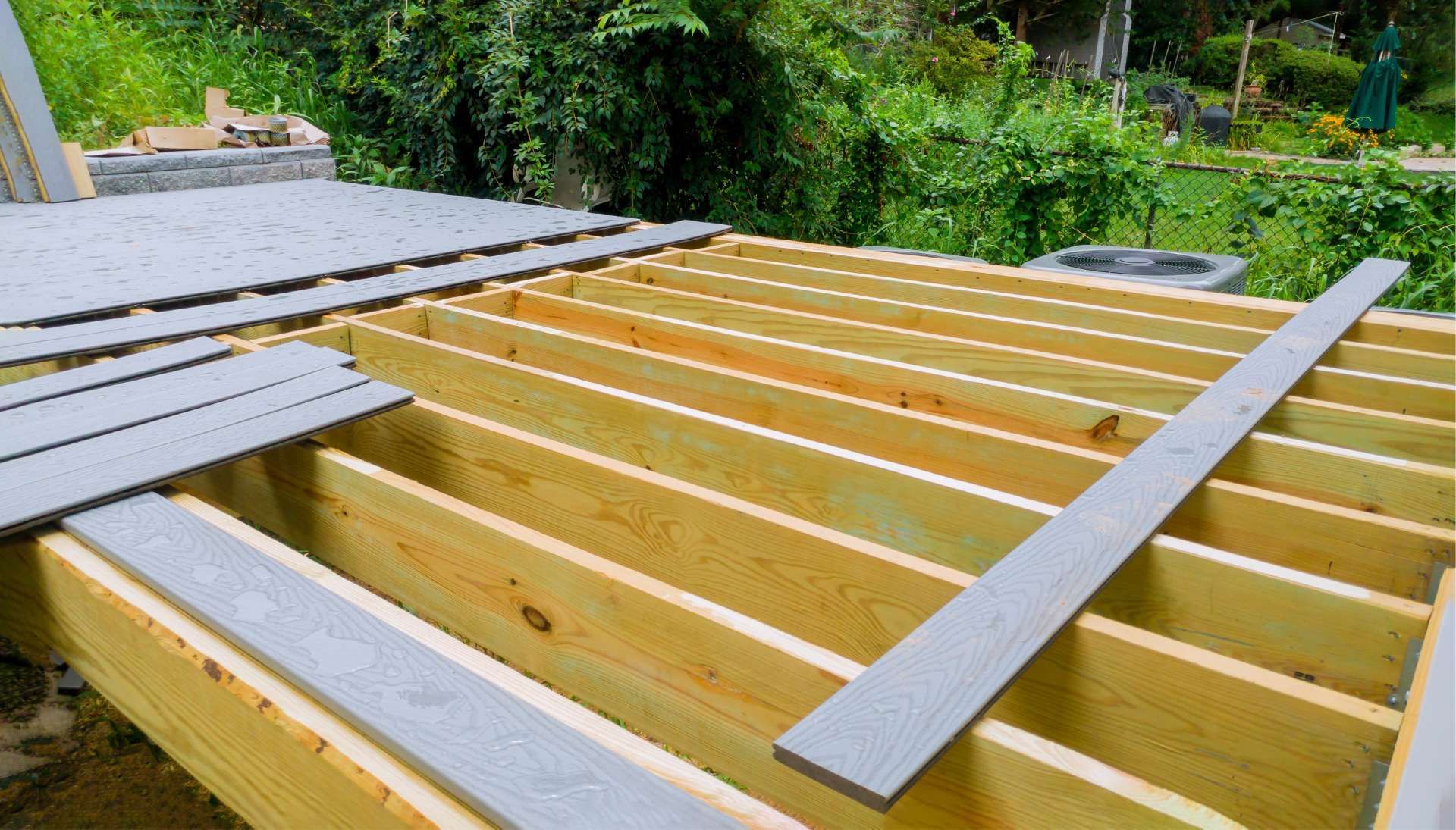 Wooden deck frame with gray composite decking boards being installed outdoors.