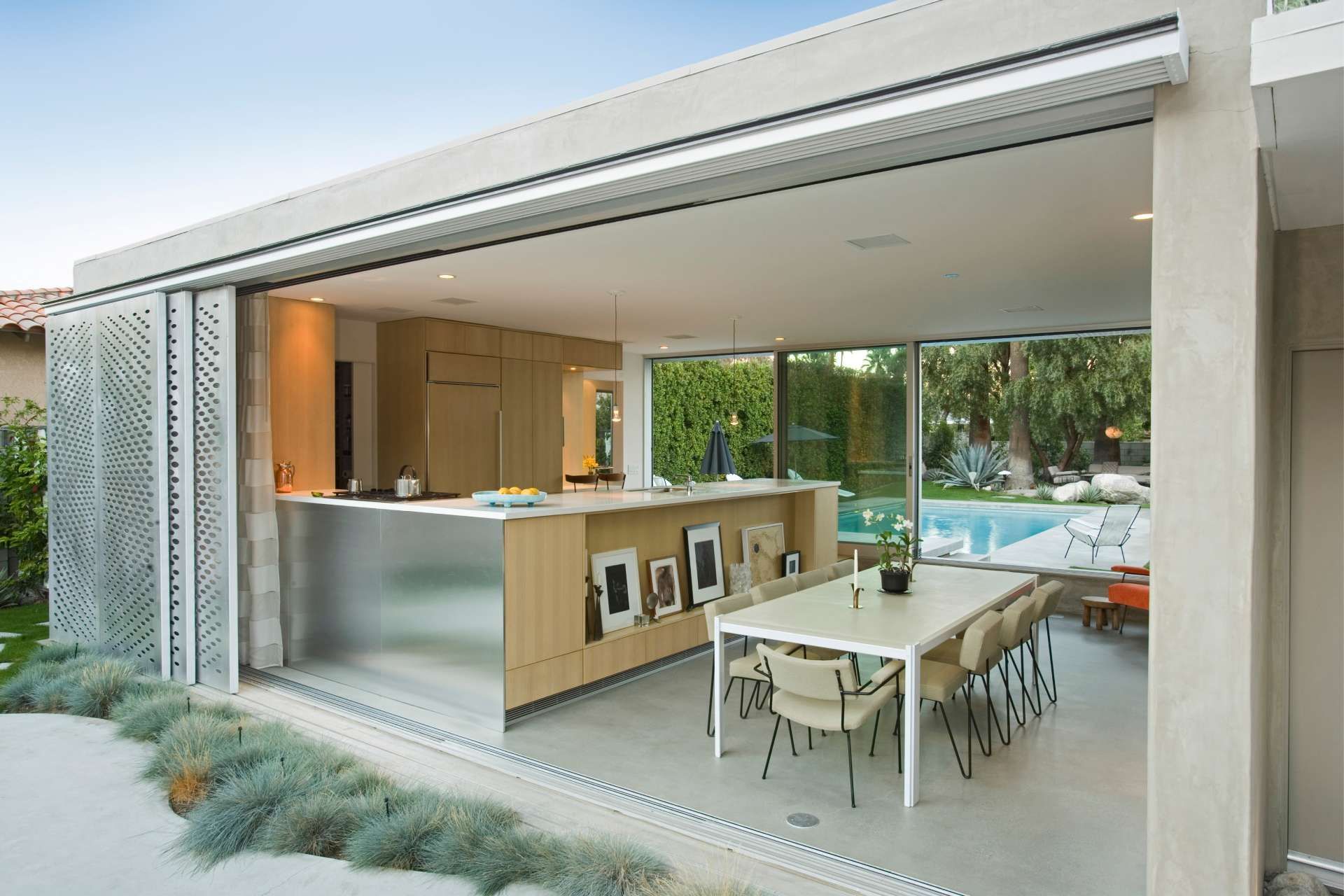 Outdoor kitchen with open sliding doors, modern design, stainless steel, light wood, and pool view.
