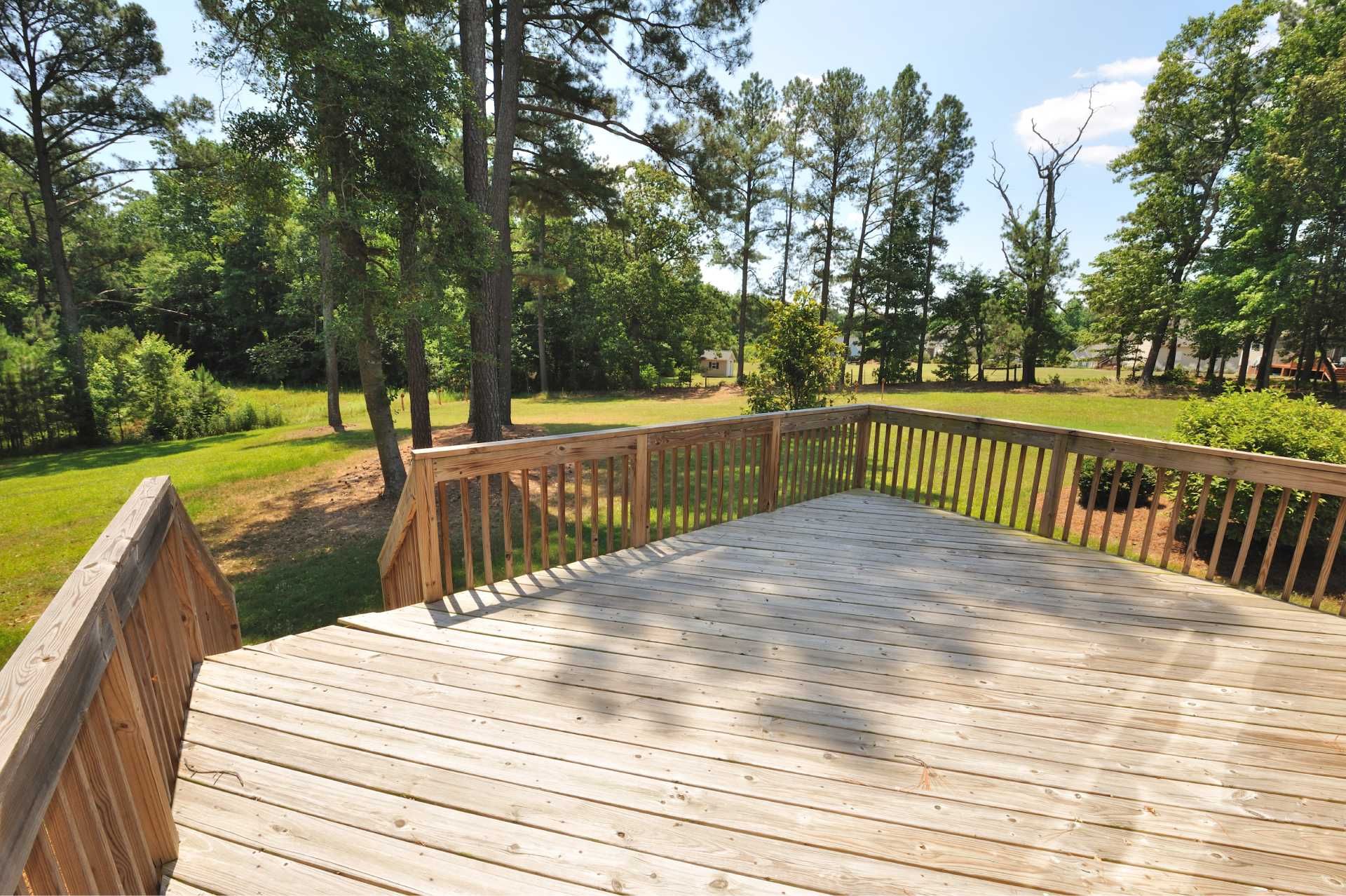 Wooden deck overlooking a grassy yard with trees under a blue sky.