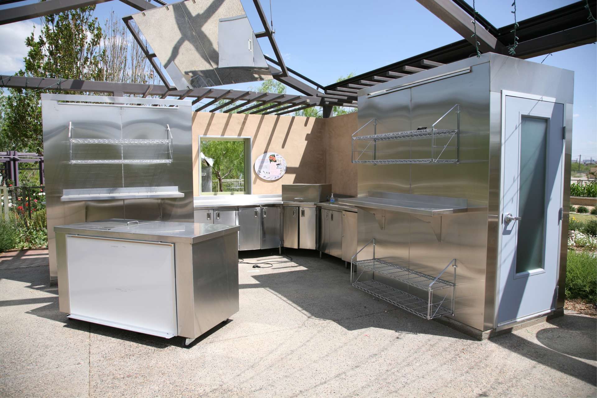 Outdoor stainless steel kitchen with countertops, shelving, and pergola roof.