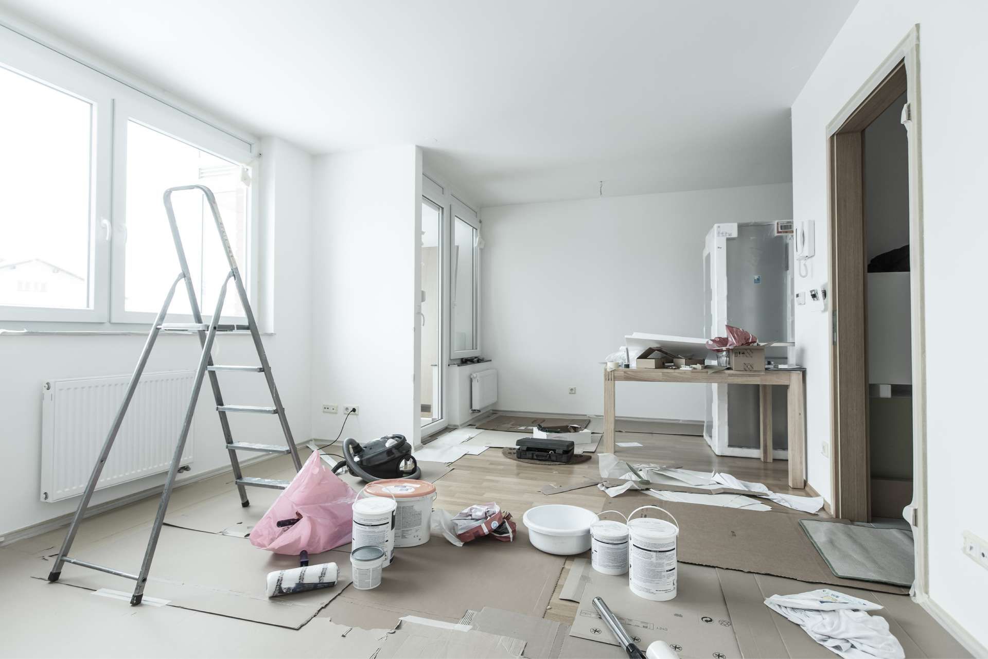 Room under renovation, ladder, paint supplies, and flooring materials on the floor.
