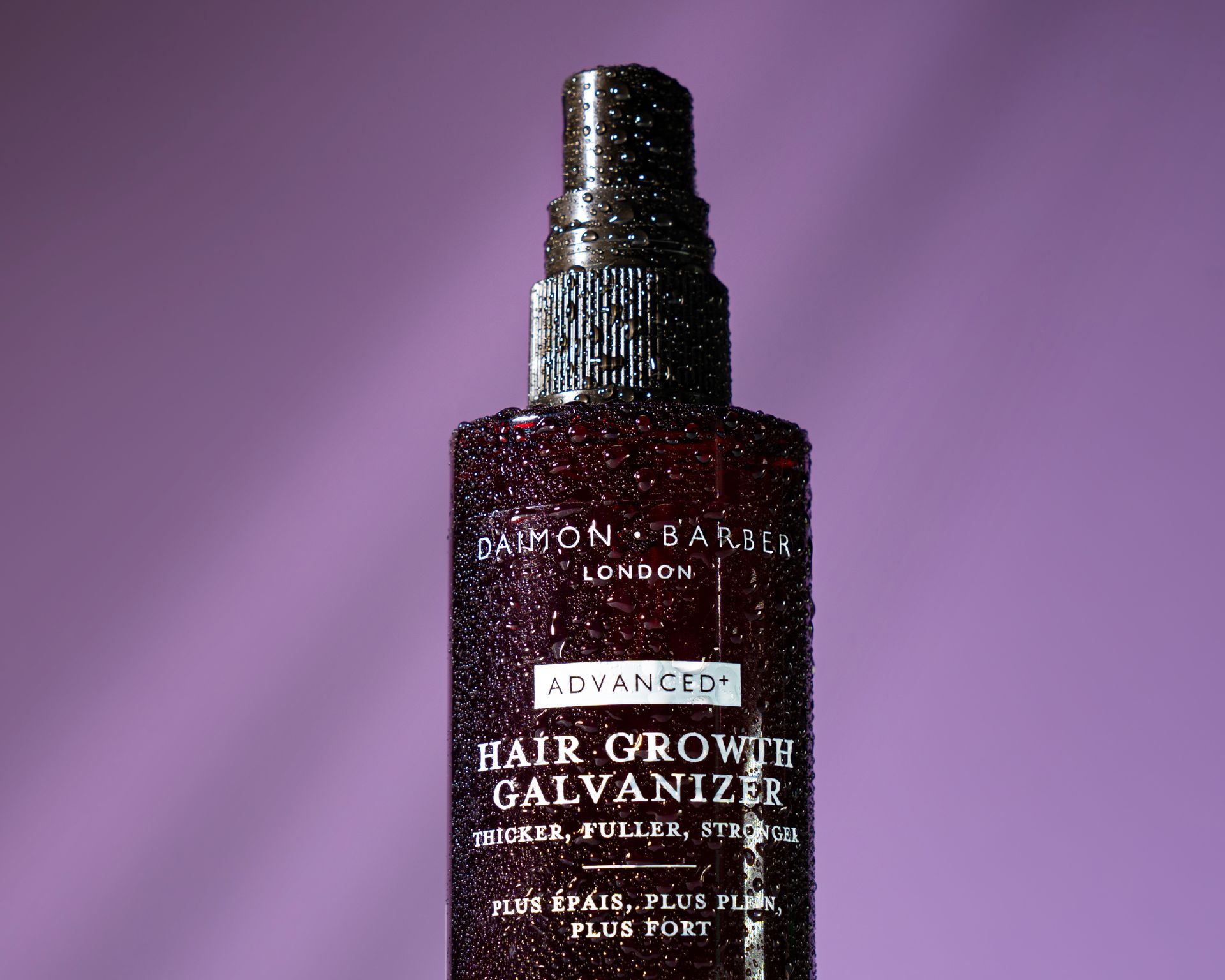 A bottle of hair growth galvanizer is sitting on a purple surface.