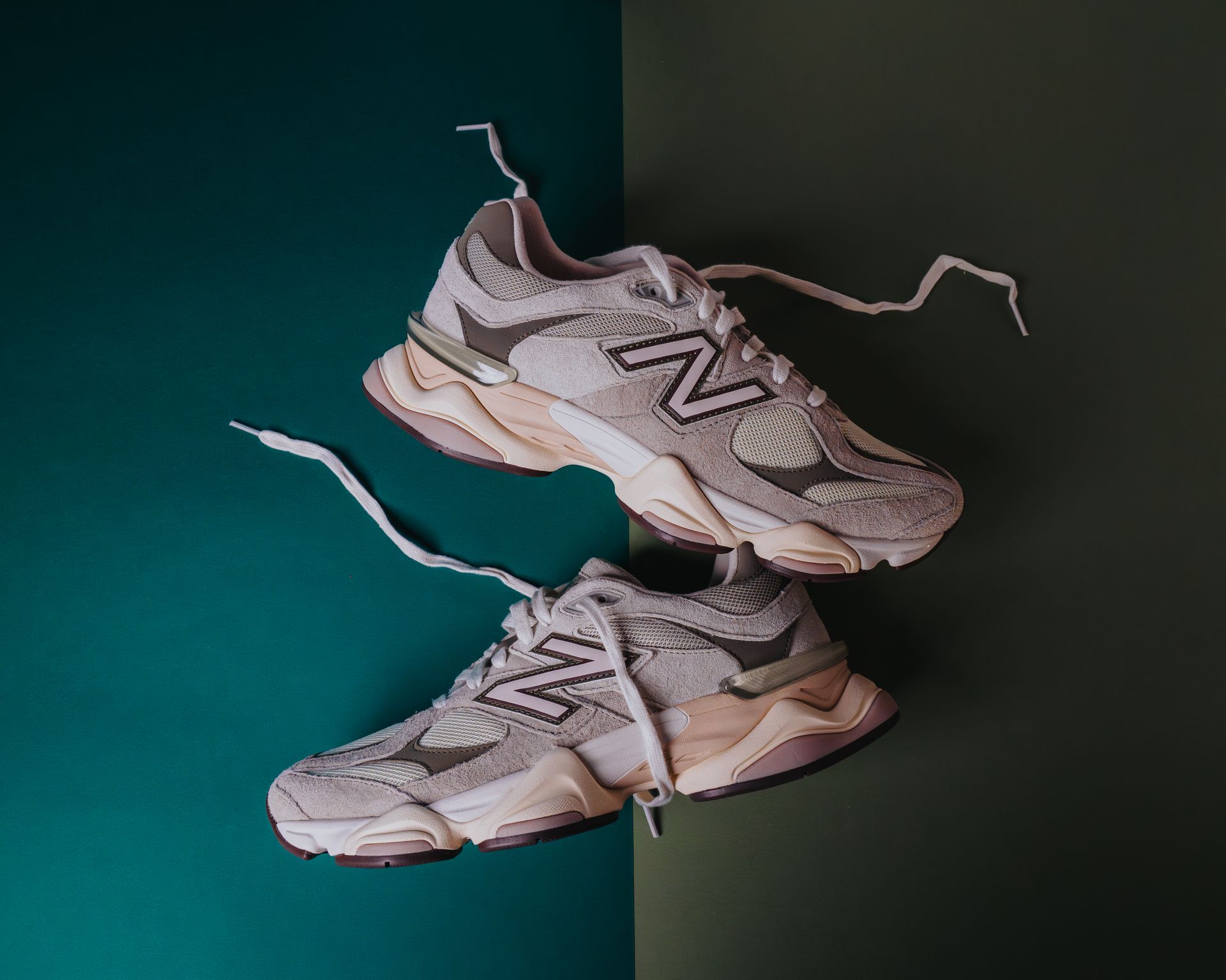A pair of new balance trainers are sitting on top of each other on a green and green surface.