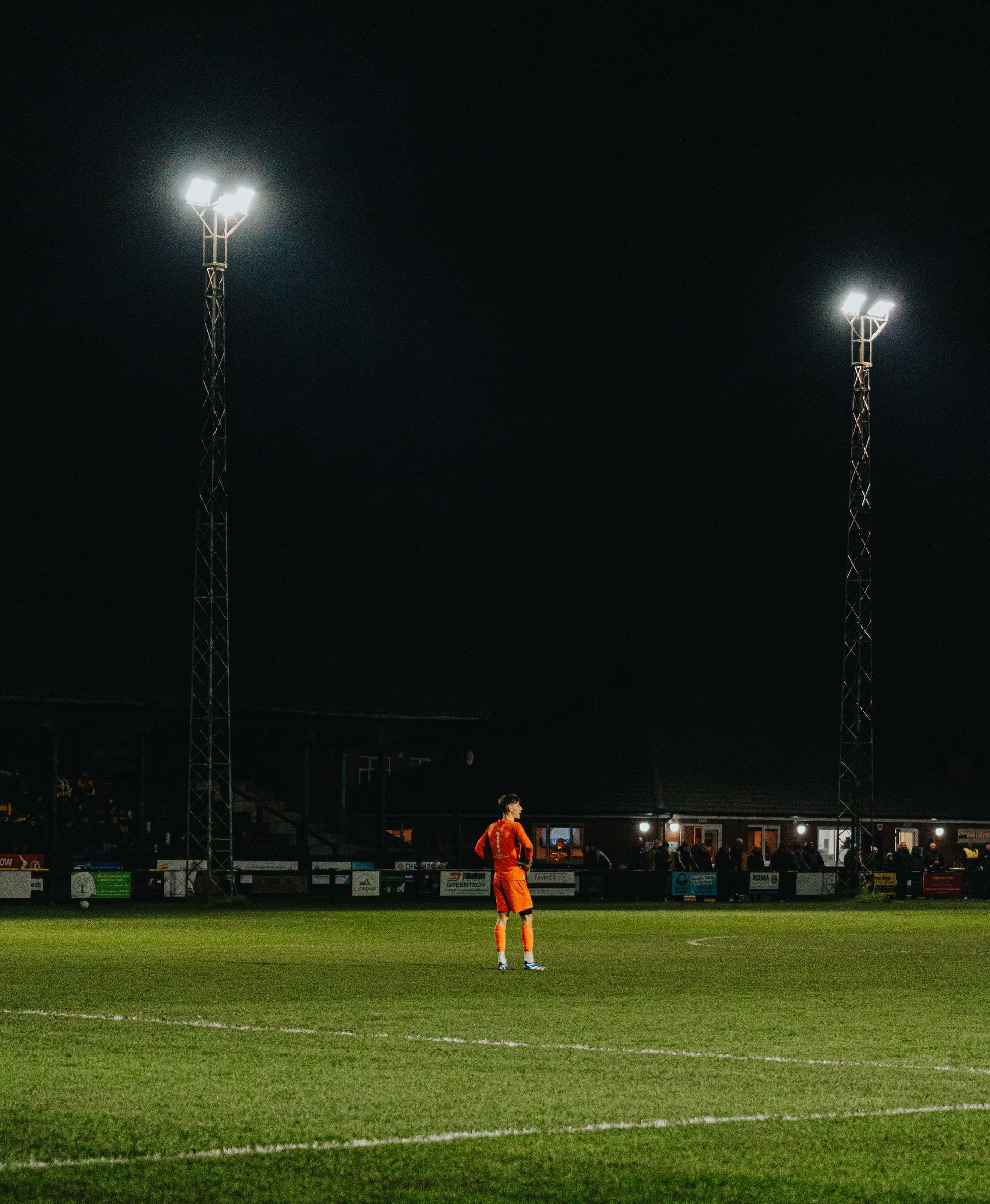 A goalkeeper  is standing on the football pitch at night, sports photography for program 