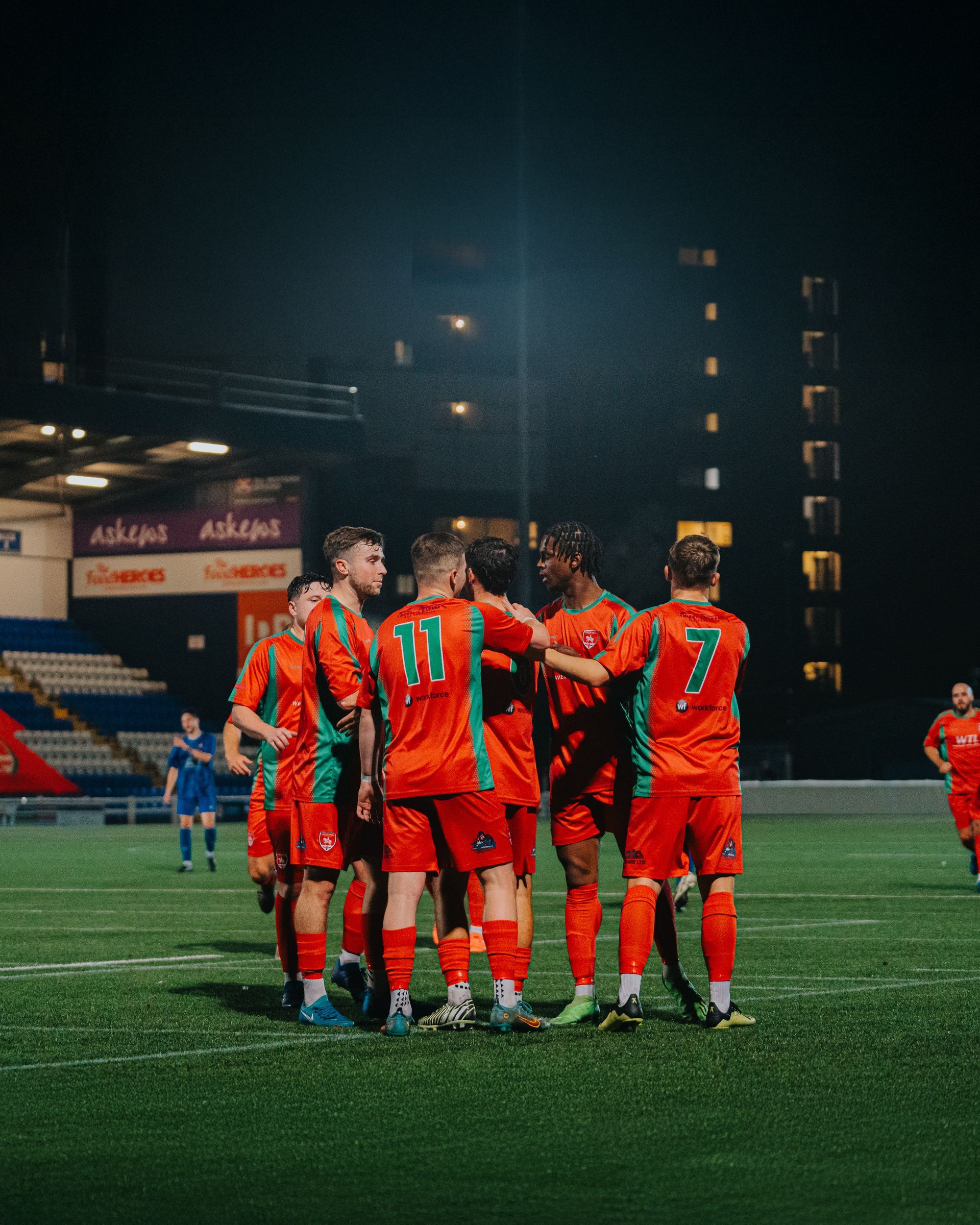 A team of football players are standing in a huddle on a field at night.