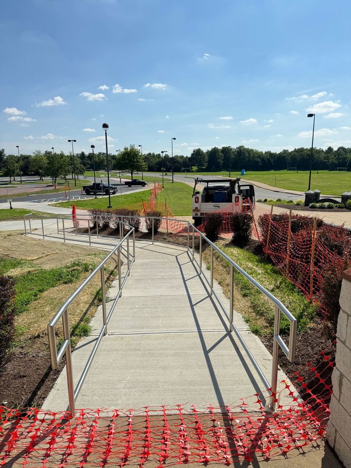 Concrete walkway with metal railings leads to a park. A truck and barriers are visible.